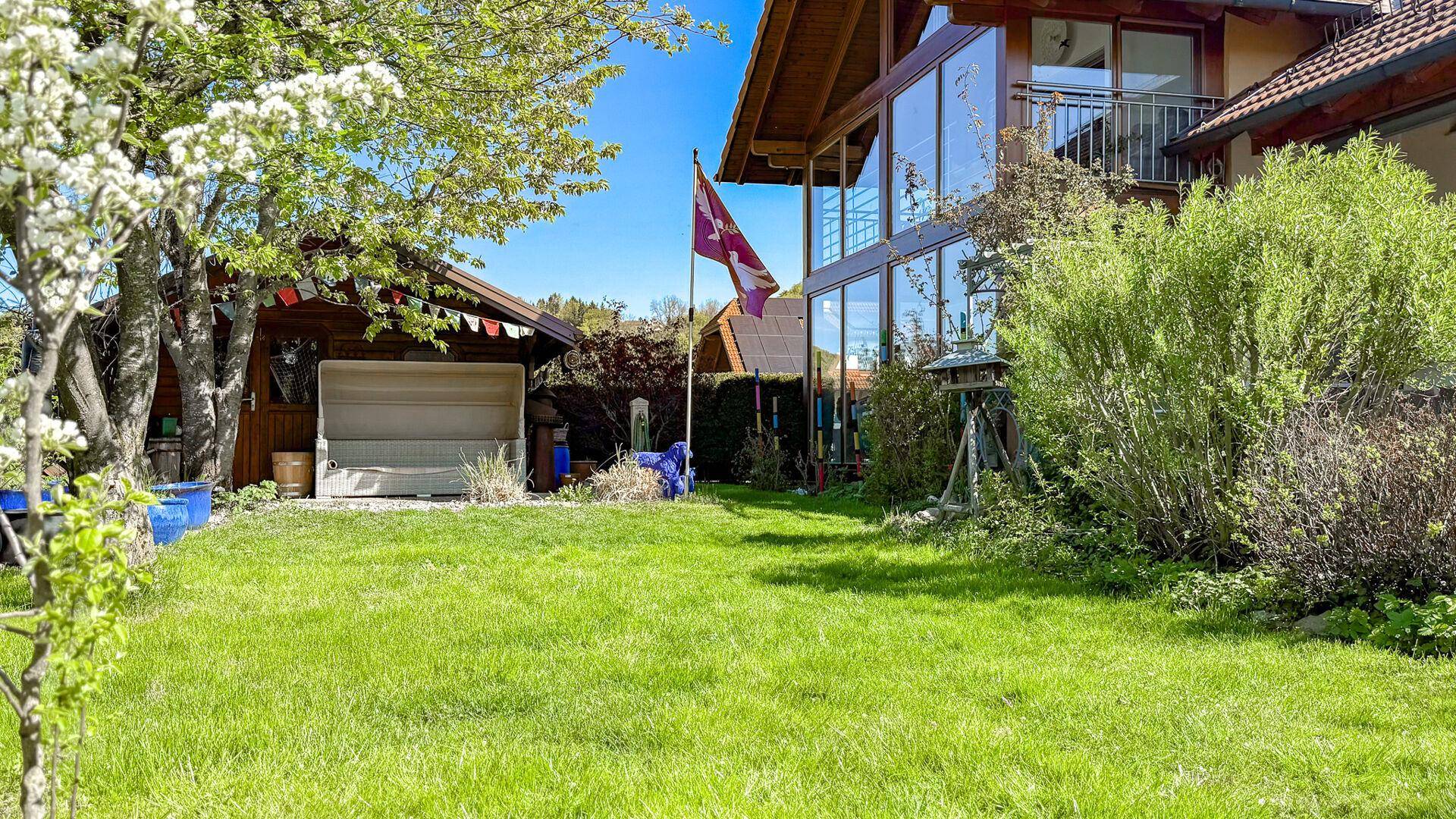 Großer grüner Garten mit Rasenfläche, Bäumen und einem Gartenhaus im Hintergrund.