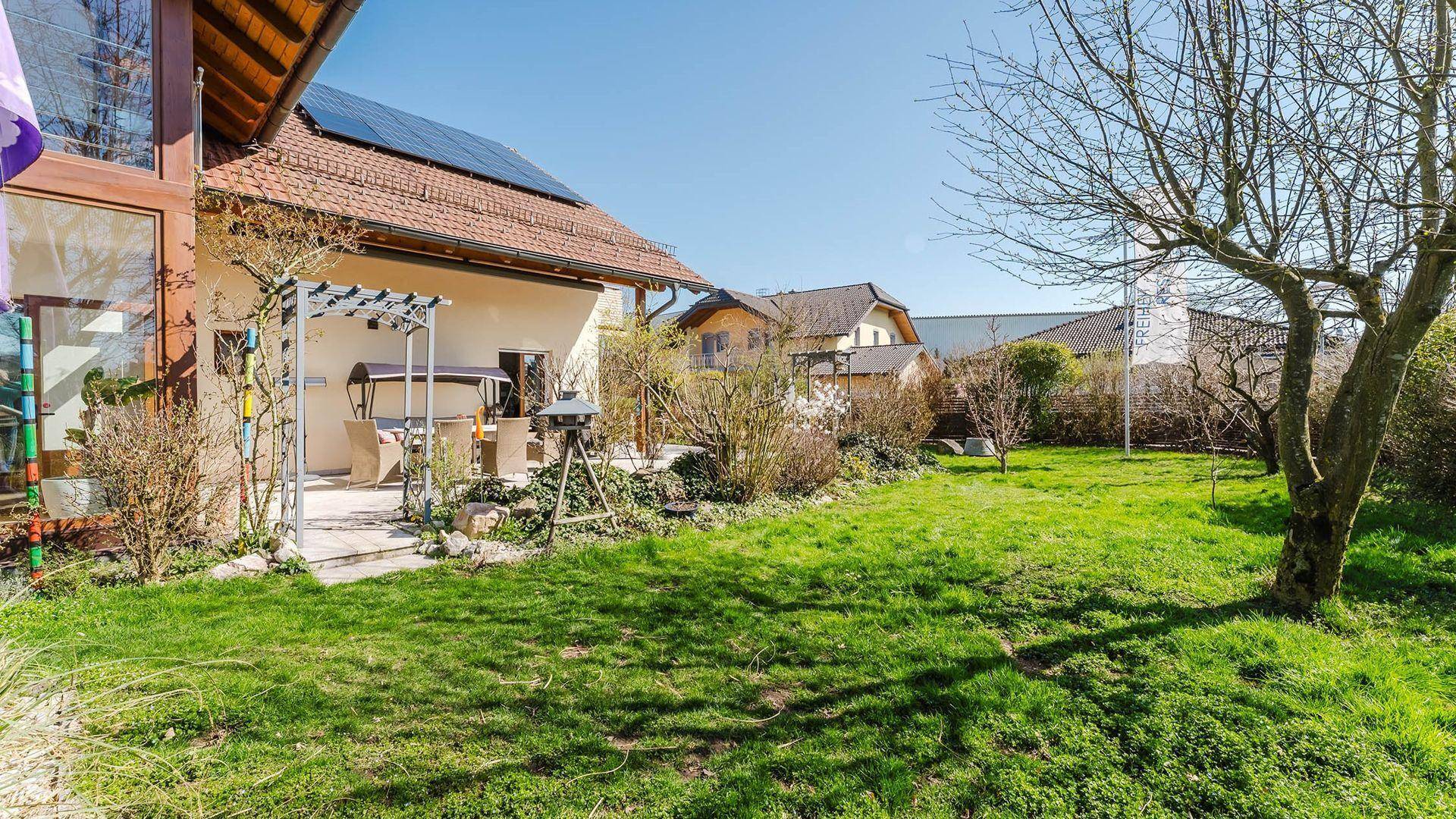 Großer Garten mit Rasenfläche und Hausfassade mit Solaranlage auf dem Dach.