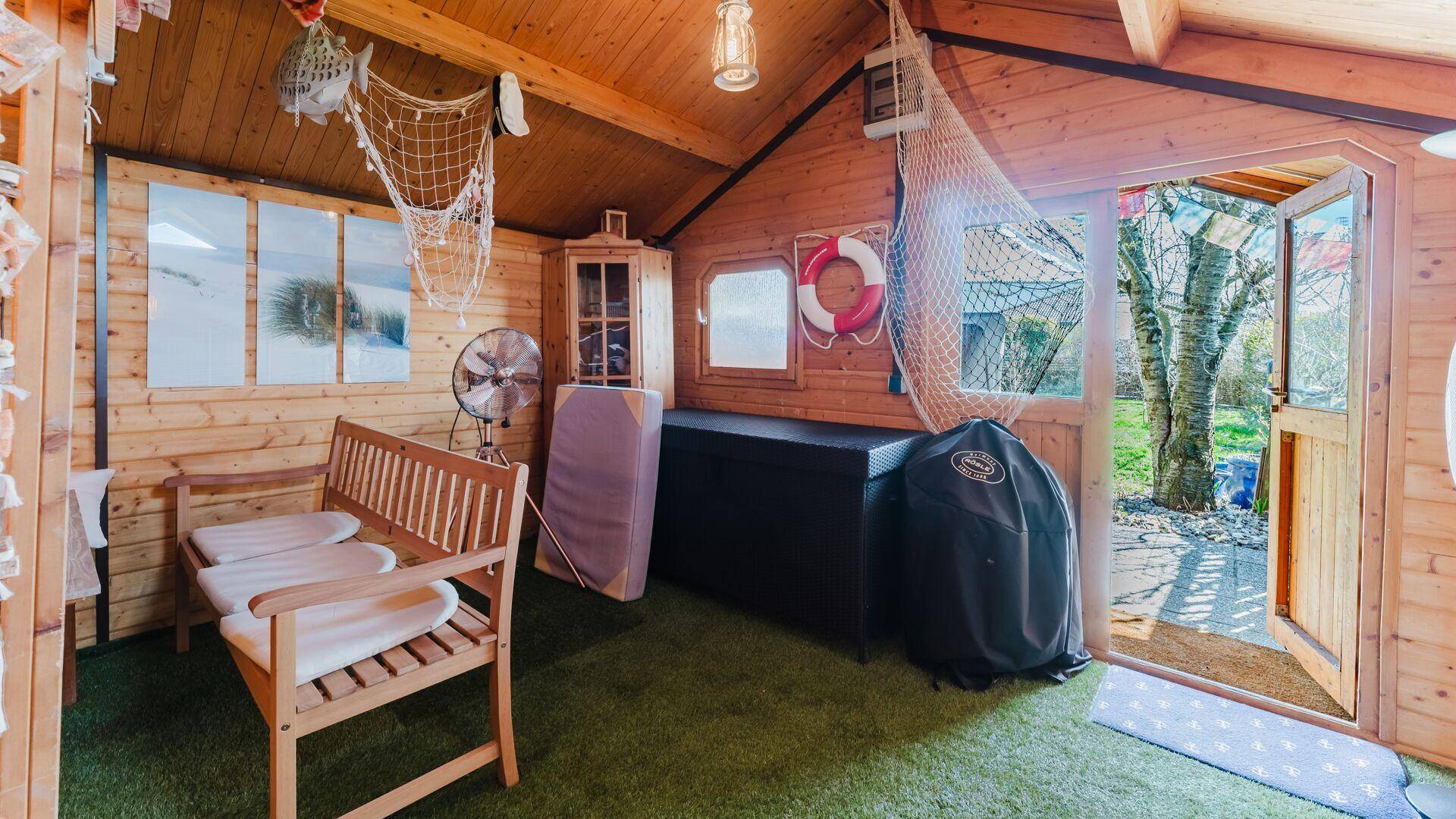 Rustikales Gartenhaus aus Holz mit maritimer Dekoration und Kunstrasenboden.