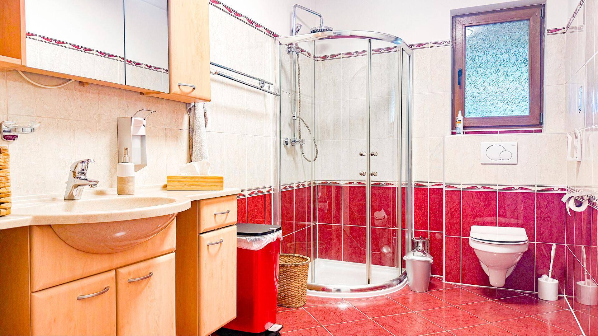 Badezimmer mit roten und weißen Fliesen, Eckdusche und wandhängendem WC.