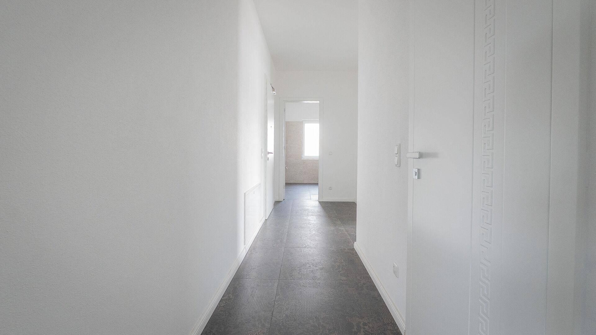 Langer, heller Flur mit dunklem Fliesenboden und mehreren Türen zu angrenzenden Räumen.