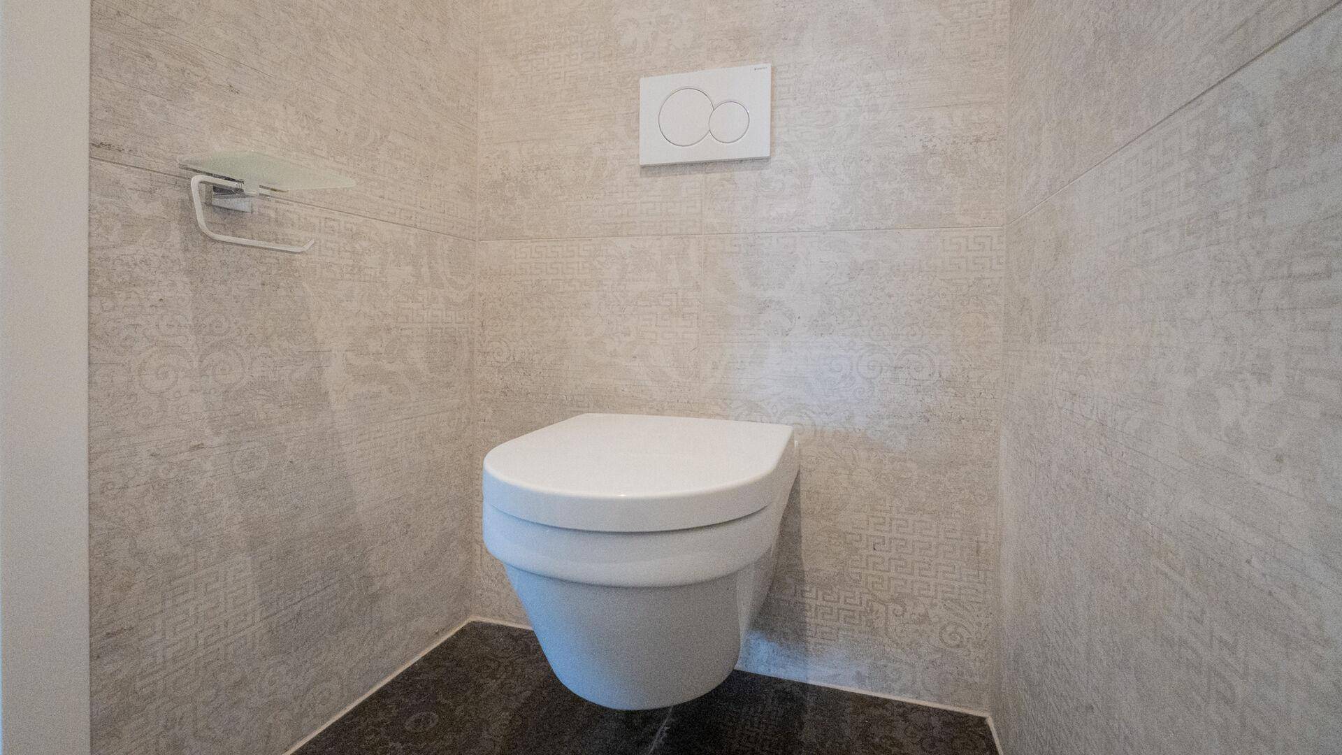 Modernes WC mit wandhängender Toilette und hellen, gemusterten Fliesen an den Wänden.