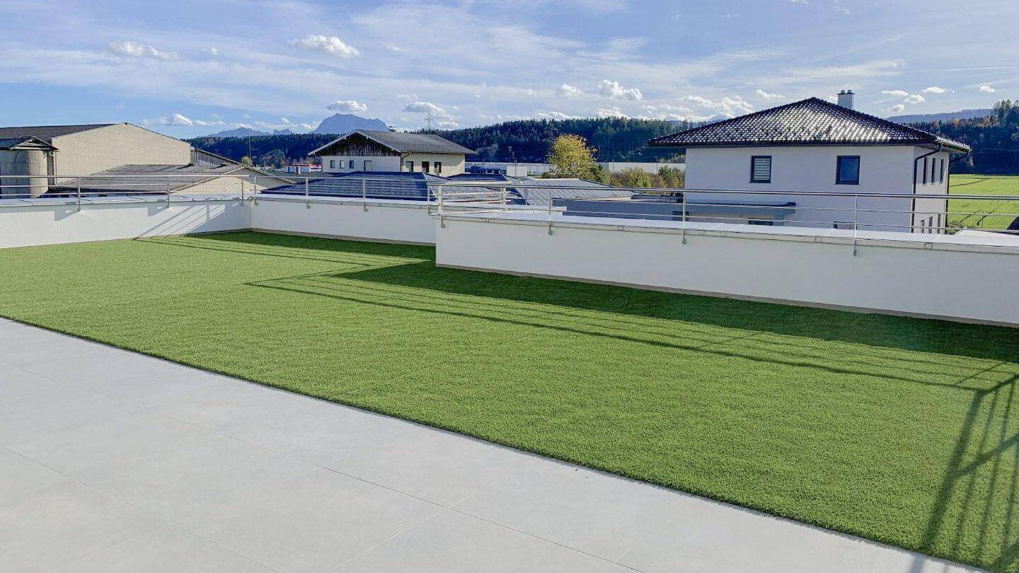 Weitläufige Dachterrasse mit Kunstrasen und Panoramablick auf die umliegende Landschaft und Berge.