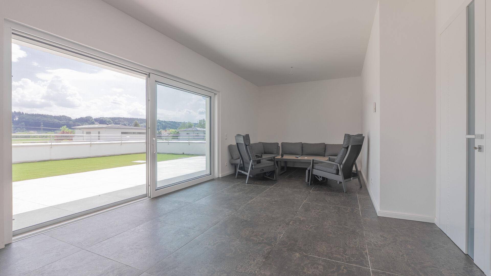 Geräumiges Wohnzimmer mit dunklen Fliesen, großen Schiebetüren und Blick auf die begrünte Dachterrasse.