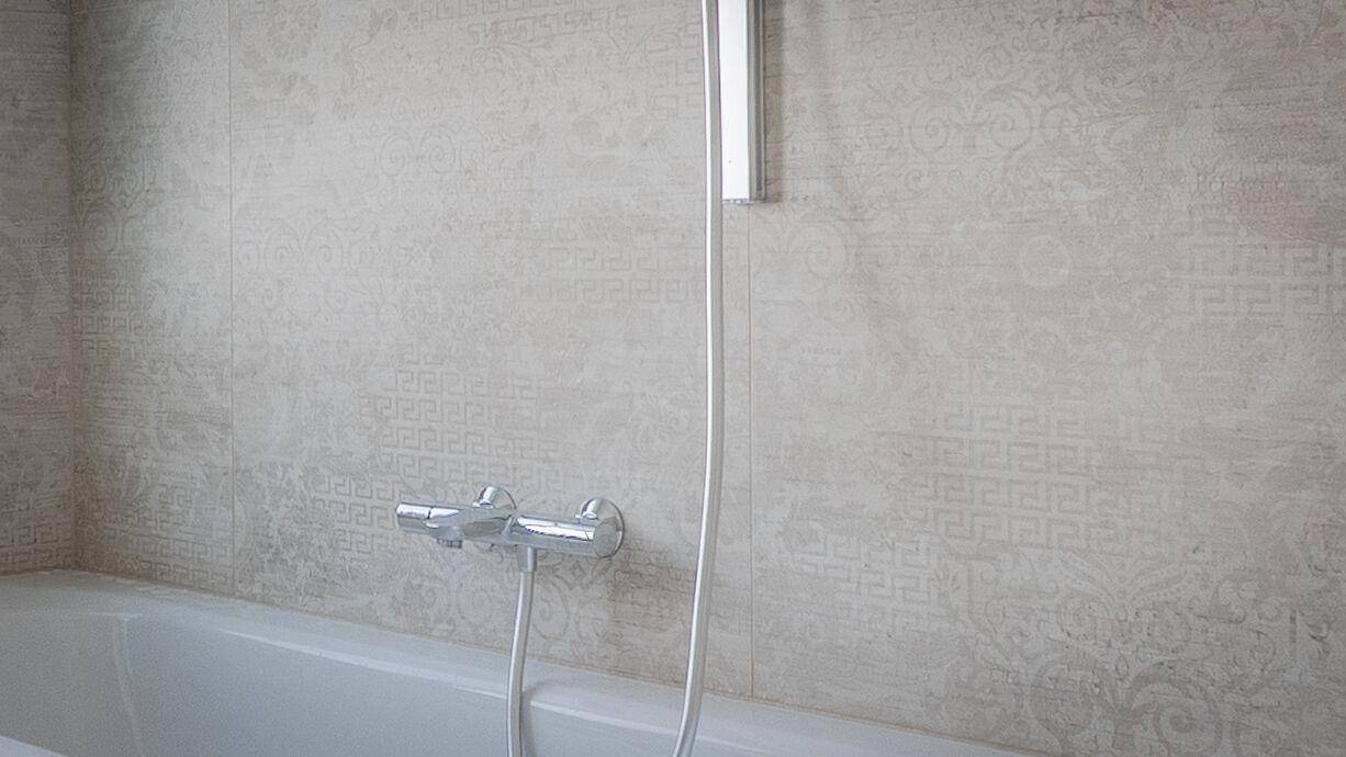 Detailaufnahme der hellen, gemusterten Wandfliesen und der modernen Armaturen über der Badewanne.