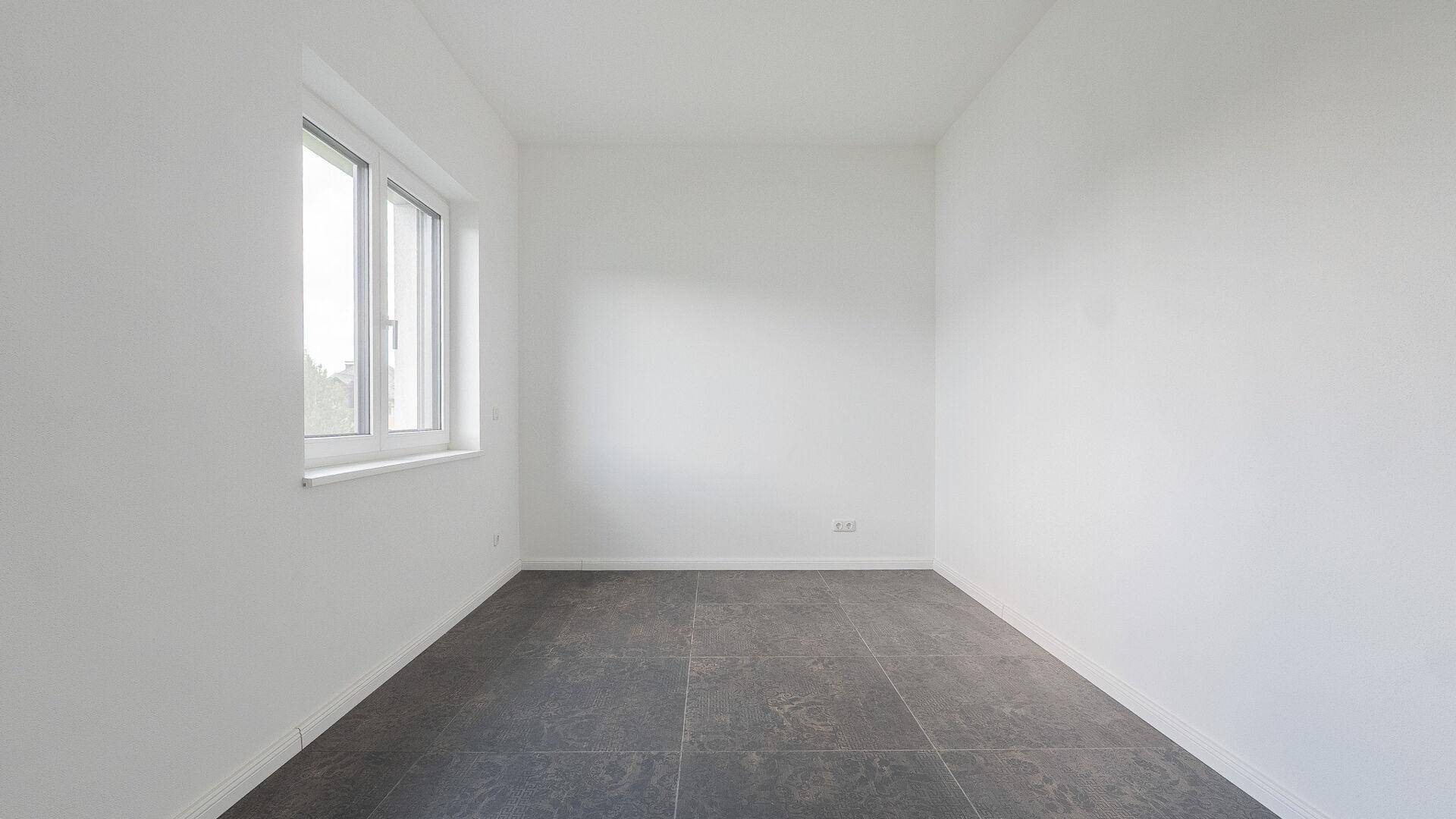 Leerer Raum mit dunklem Fliesenboden und einem Fenster, bereit für die persönliche Einrichtung.