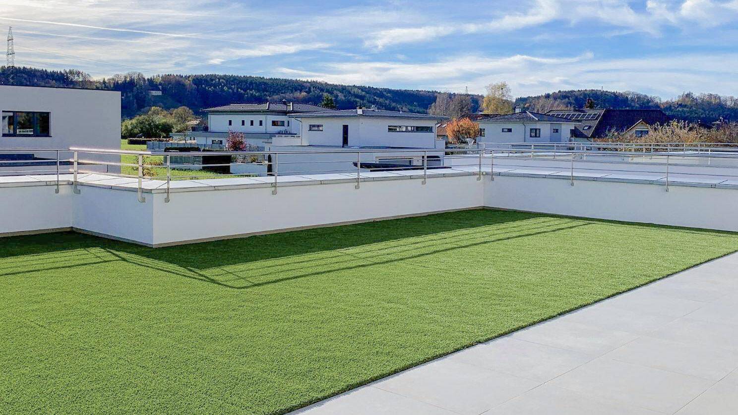 Weitläufige Dachterrasse mit Kunstrasen und Panoramablick auf die umliegende Landschaft und Berge.