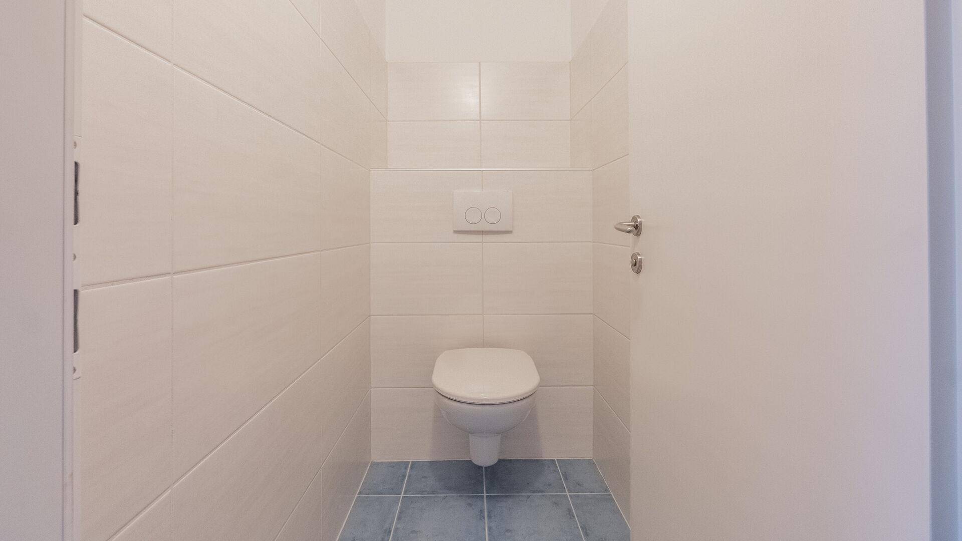 Separate Toilette mit Wand-WC und hellen Fliesen an den Wänden, ergänzt durch einen blauen Boden.