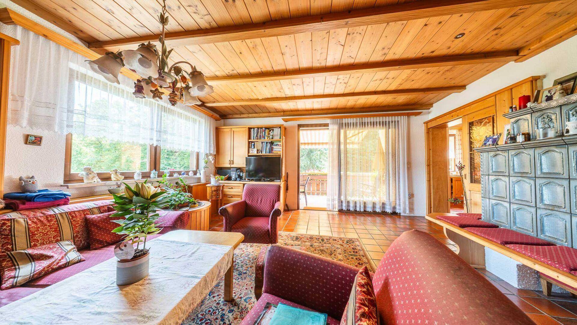 Gemütliches Wohnzimmer im Landhausstil mit Holzbalkendecke, Kachelofen und Zugang zum Balkon.