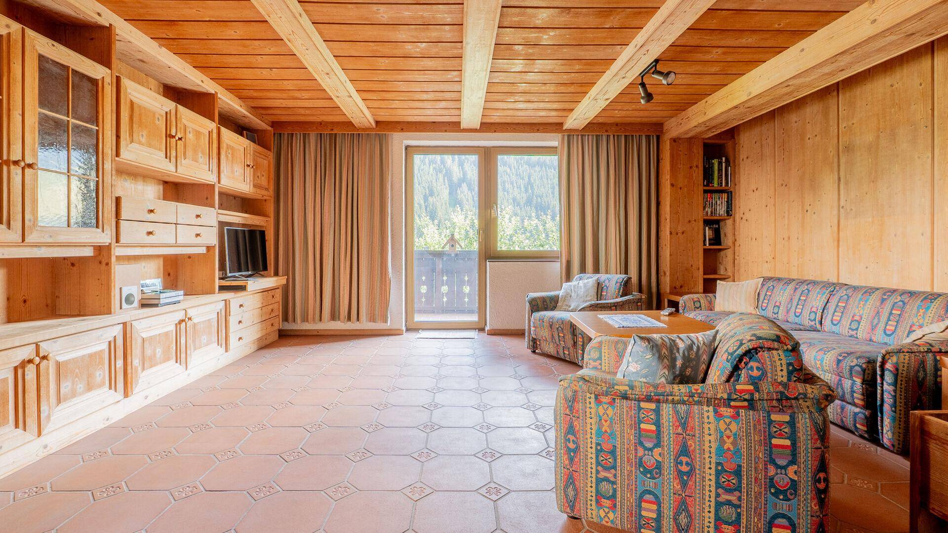 Geräumiges Wohnzimmer mit Holzbalkendecke, Terrakottafliesen und einer großen Holzschrankwand.