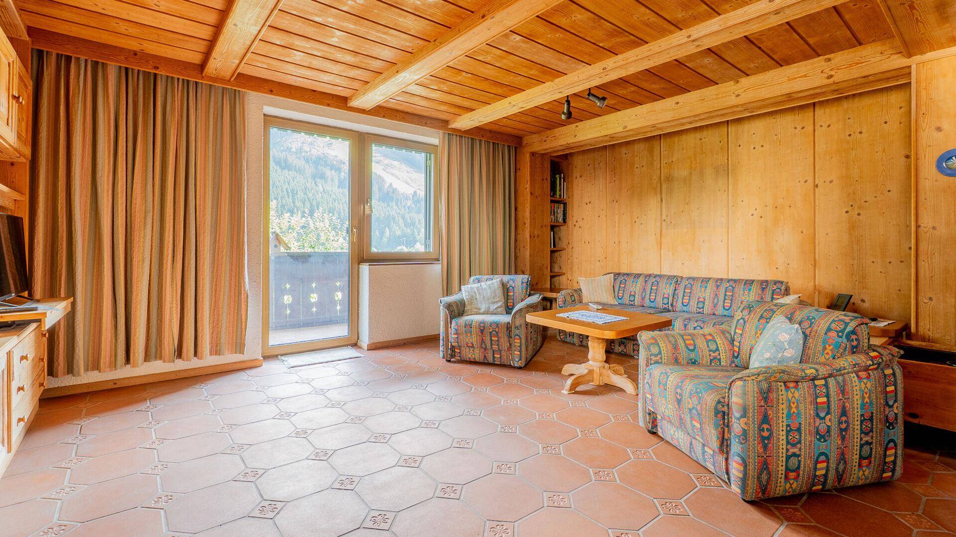 Gemütliches Wohnzimmer im alpinen Stil mit Holzbalkendecke, Terrakottafliesen und traditionellen Möbeln.