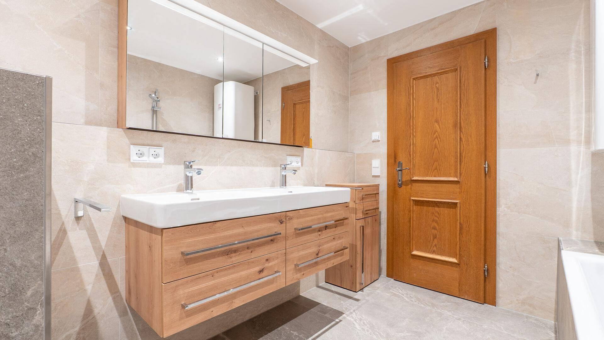 Modernes Badezimmer mit Doppelwaschbecken, Holzunterschrank und großem Spiegelschrank.
