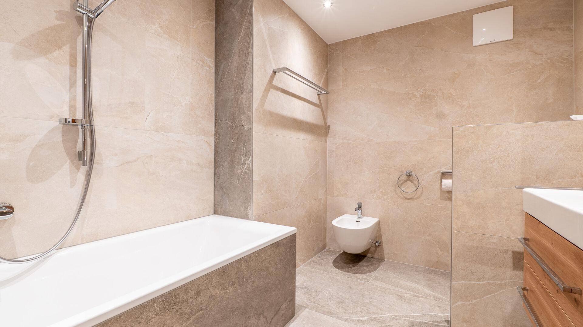 Modernes Badezimmer mit beigefarbenen Fliesen, Badewanne mit Duschfunktion und Bidet.
