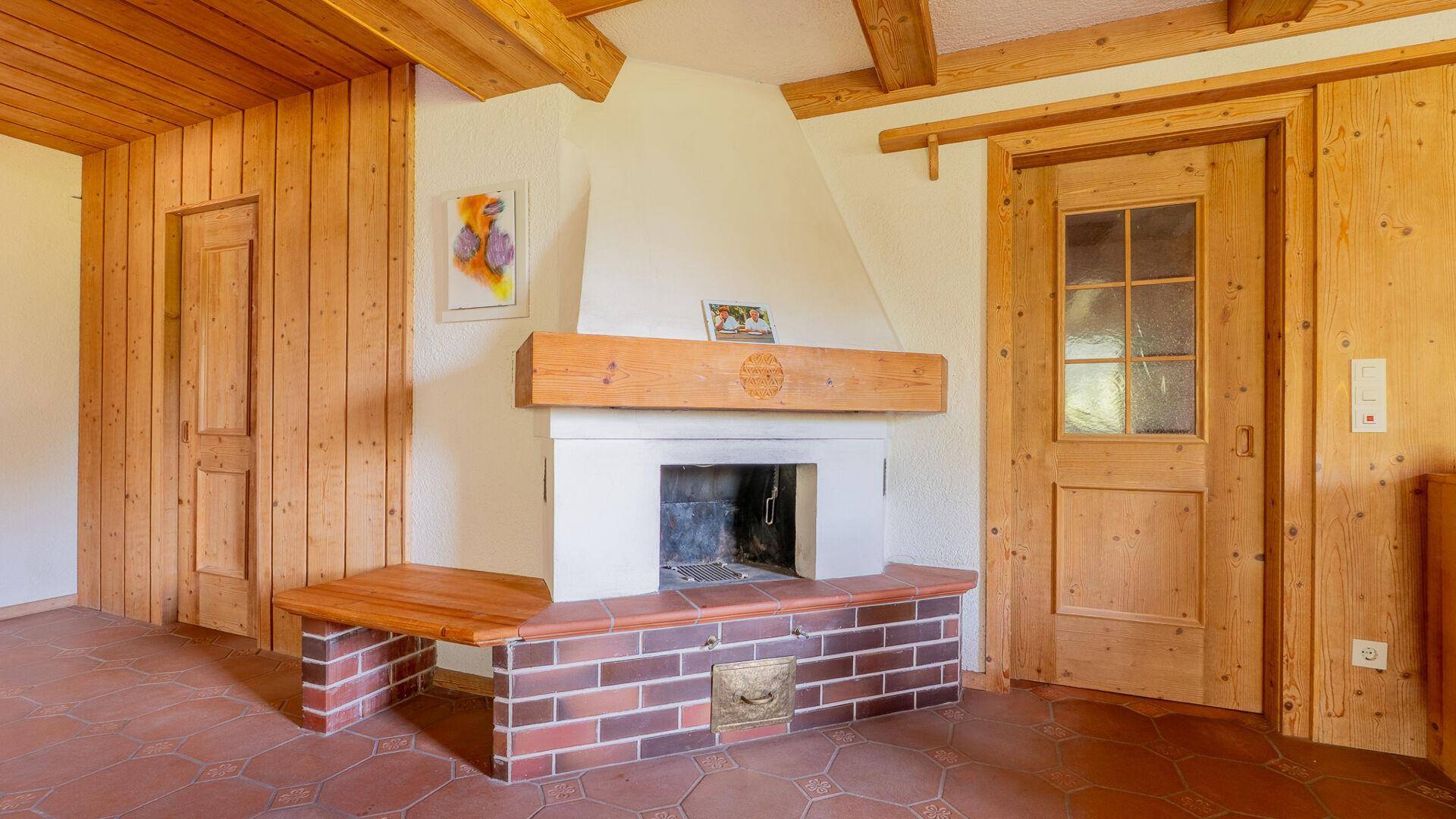 Traditioneller Kamin mit gemauertem Sockel und Holzbalken in einem Raum mit Holzvertäfelung.