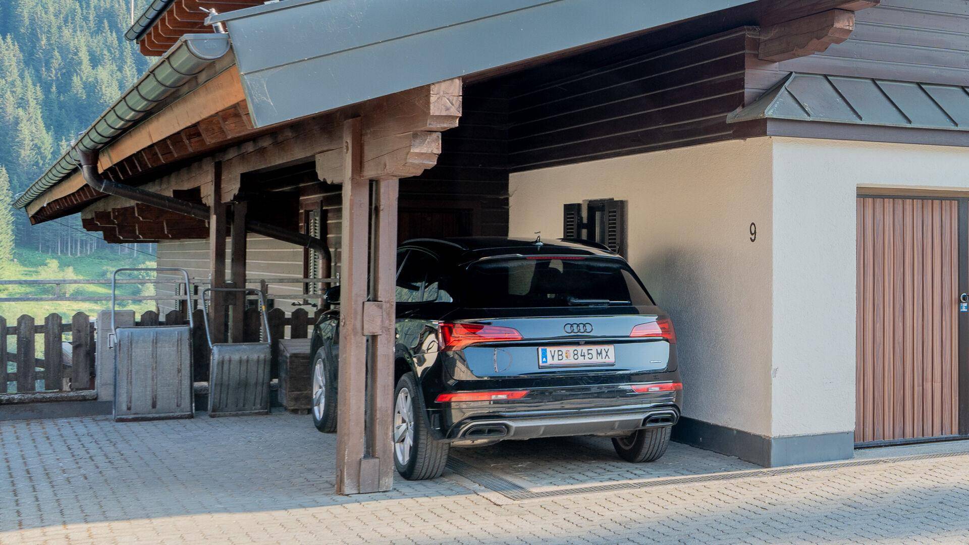 Überdachter Stellplatz für ein Fahrzeug neben einem traditionellen Gebäude mit Holzverkleidung.