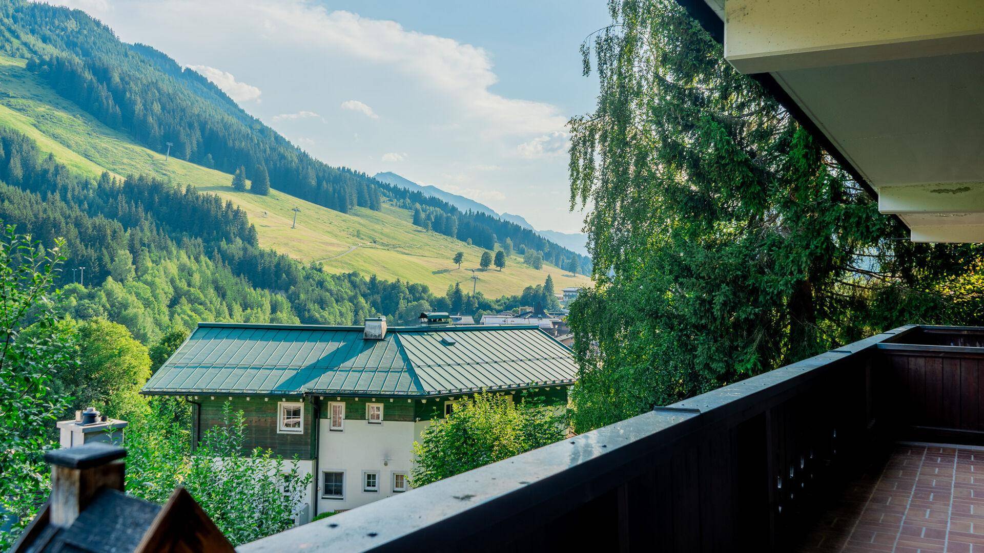 Panoramablick vom Balkon auf die umliegenden grünen Berge und ein traditionelles Haus mit grünem Dach.