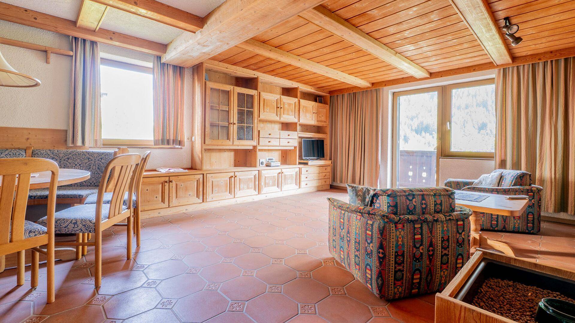Heller Wohn- und Essbereich im alpinen Stil mit Holzbalkendecke, Terrakottafliesen und traditionellen Holzmöbeln.