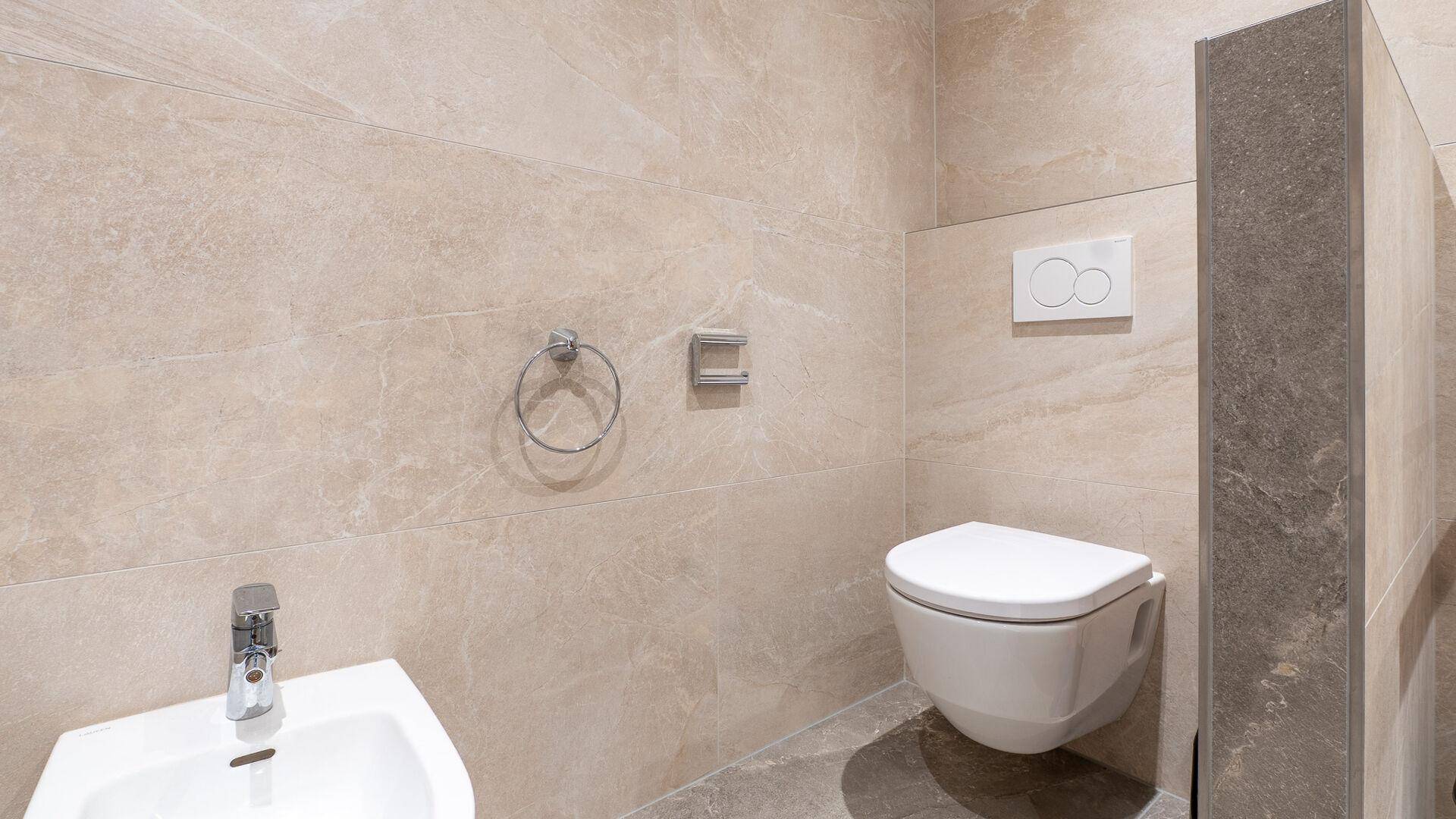 Modernes WC mit Wandtoilette und Bidet in einem hell gefliesten Badezimmer.