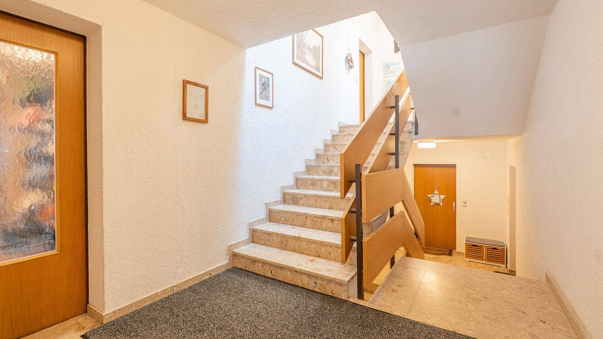 Heller Treppenaufgang mit Marmorstufen und Holzgeländer in einem Mehrfamilienhaus.