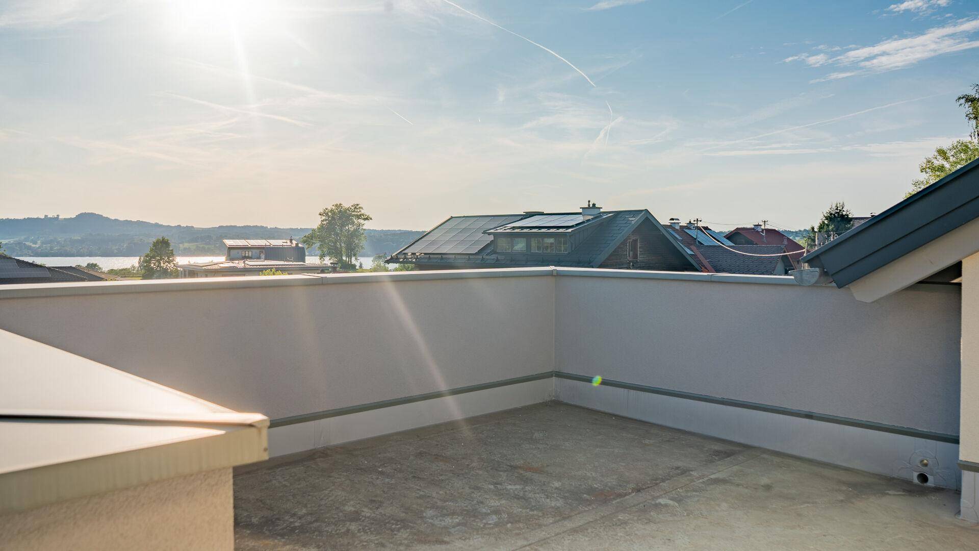 Geräumige, unmöblierte Terrasse mit Panoramablick auf den See und die umliegende Landschaft unter blauem Himmel.