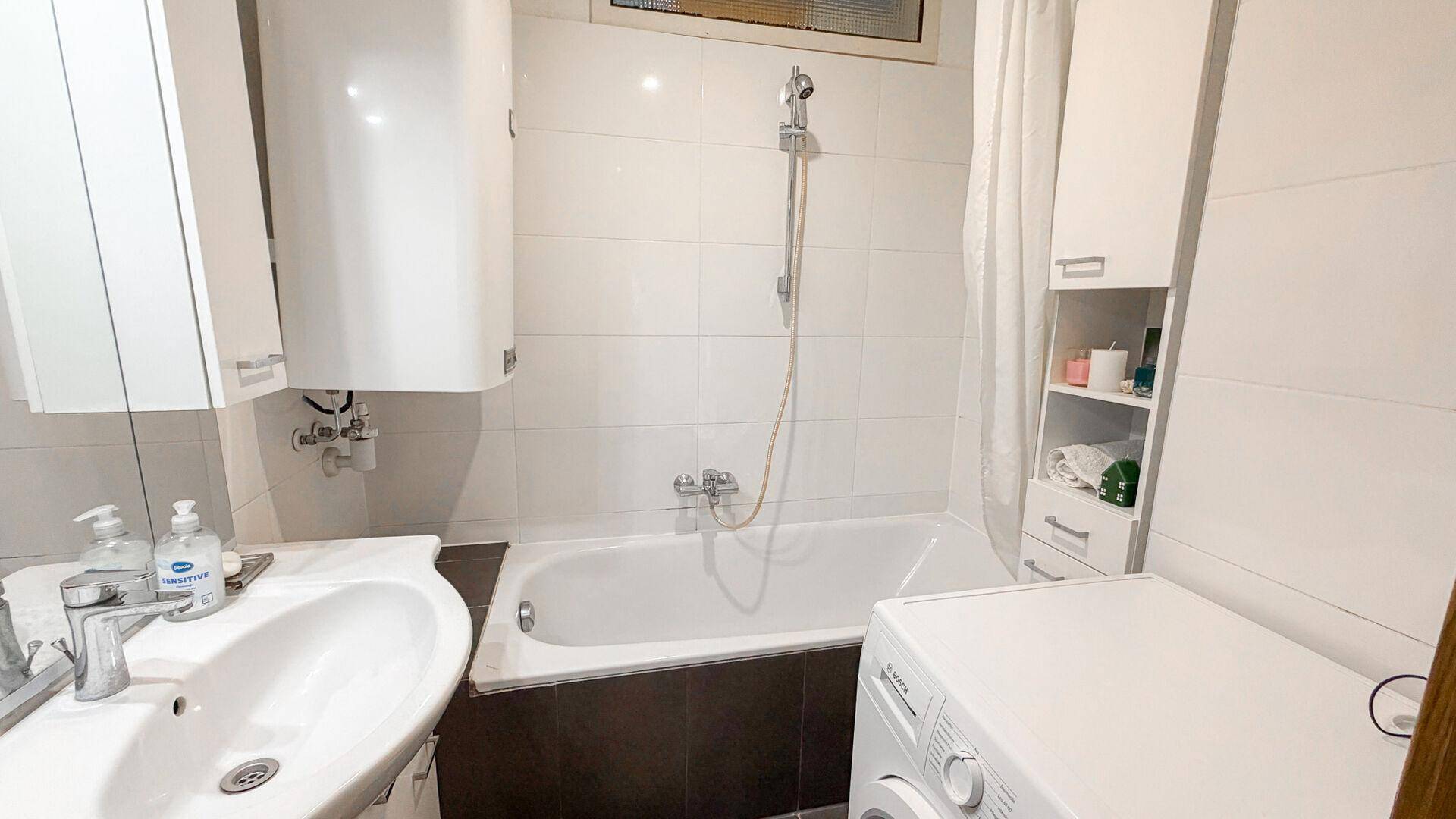 Funktionales Badezimmer mit Badewanne, Waschbecken und Waschmaschine, hell gefliest.