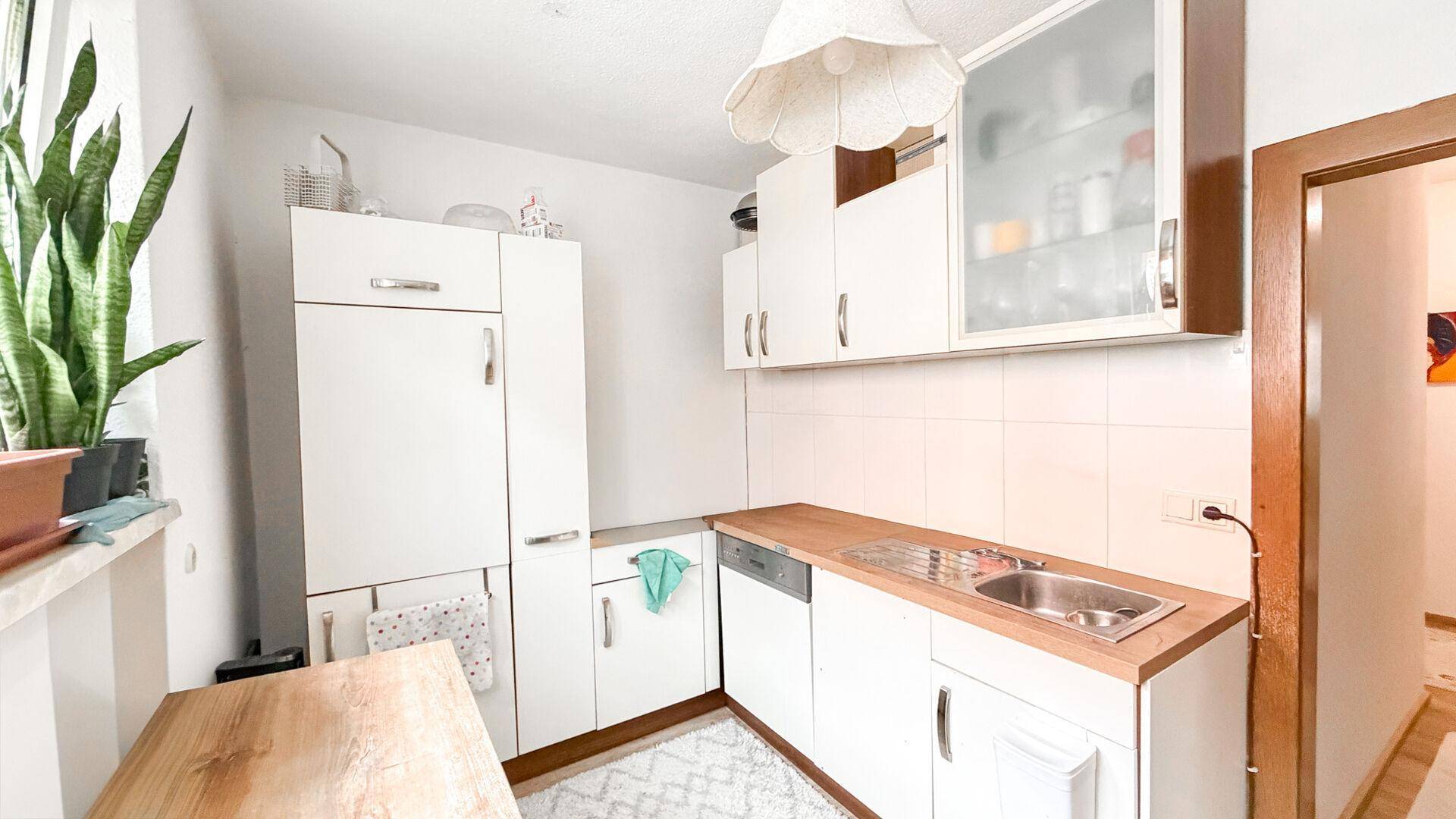 Kompakte Küche mit weißen Schränken, Holz-Arbeitsplatte und integriertem Kühlschrank.