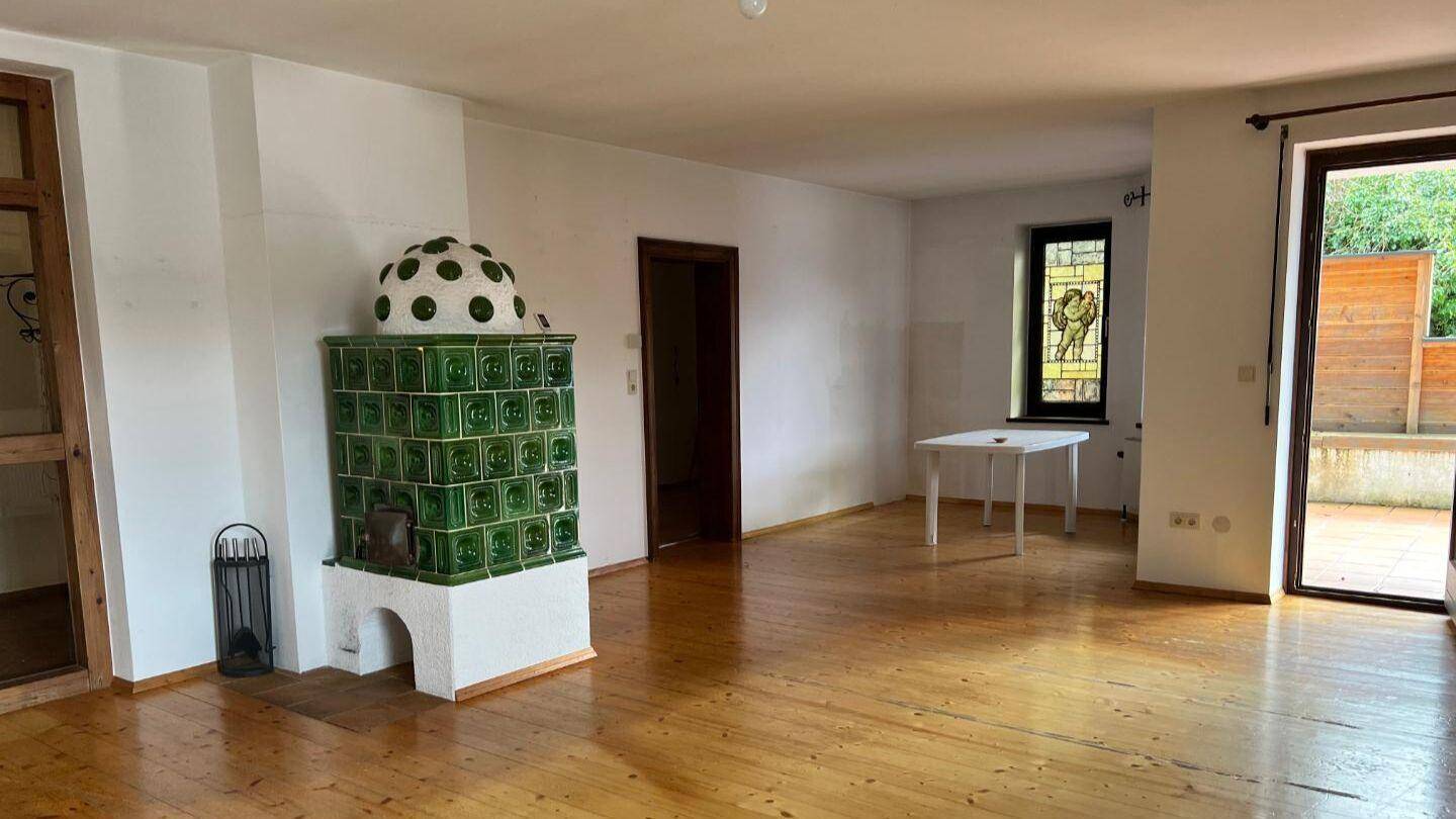 Geräumiges Wohnzimmer mit traditionellem Kachelofen, Holzboden und Zugang zur Terrasse.