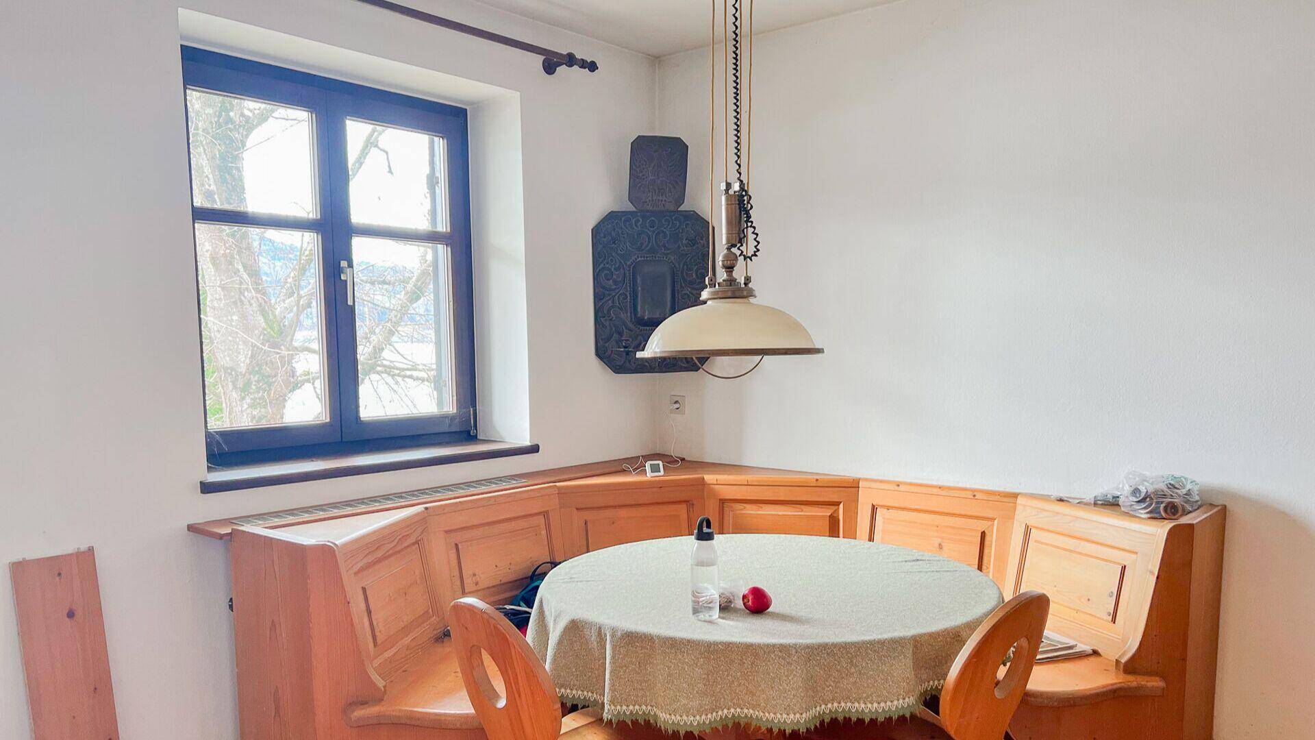 Gemütliche Essecke mit Holzbänken, rundem Tisch und Blick nach draußen durch das Fenster.
