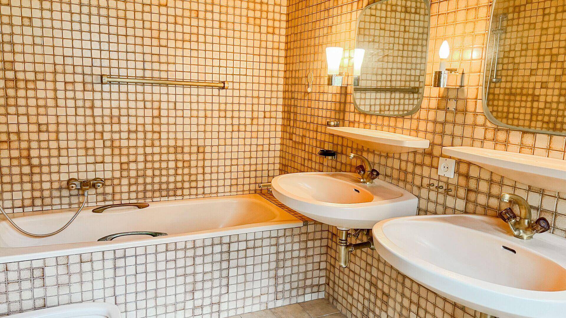 Badezimmer mit kleinen braunen Fliesen, zwei Waschbecken und einer Badewanne.