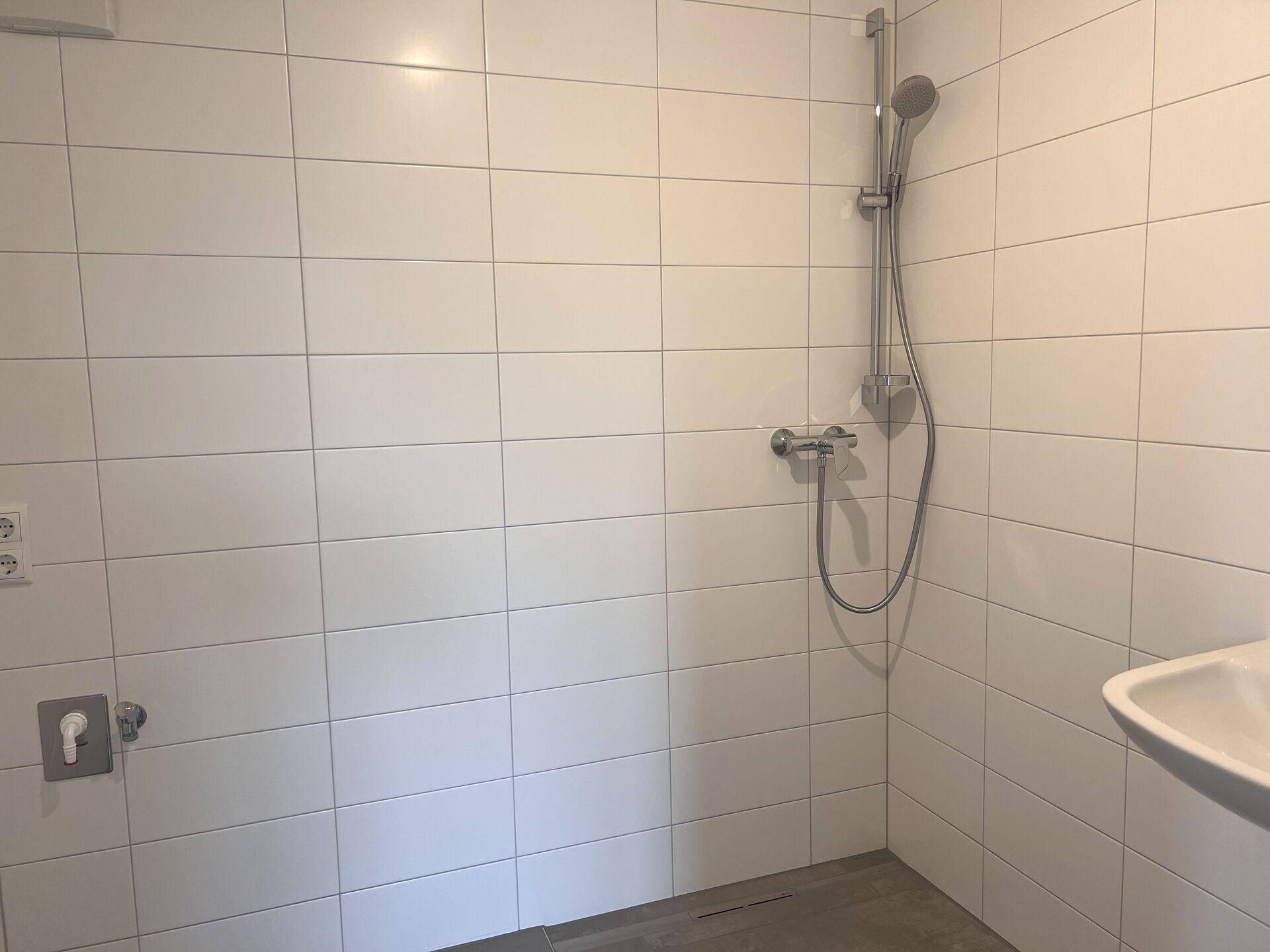 Modernes Badezimmer mit weißen Fliesen, einer Duschvorrichtung und einem Waschbecken.