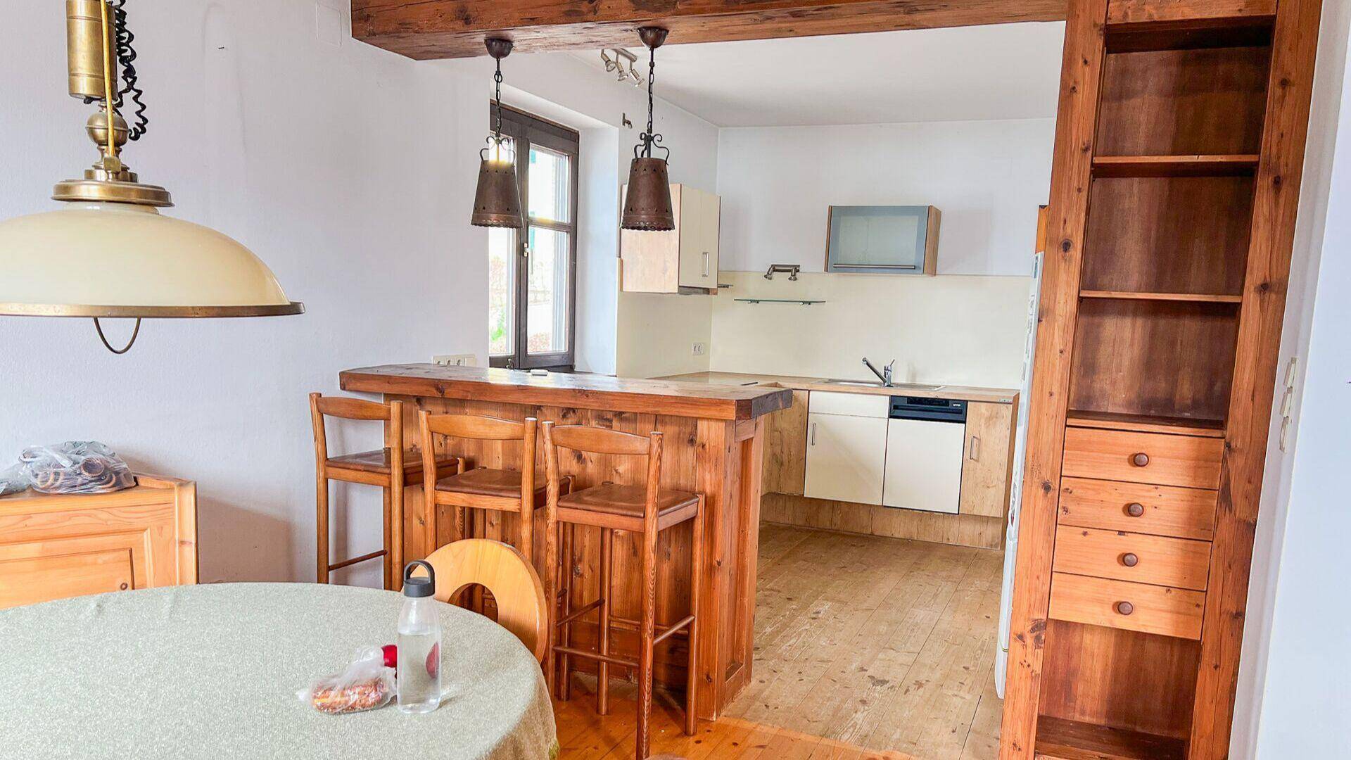 Küche mit rustikaler Holztheke, einfachen Einbauschränken und offenem Übergang zum Essbereich.