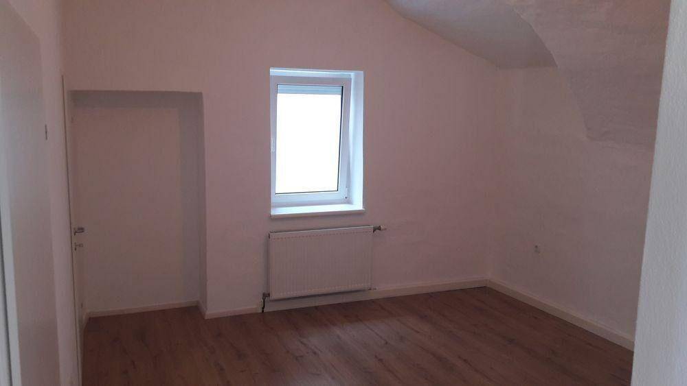 Helles Zimmer im Dachgeschoss mit Holzboden und einem Fenster, bereit zur individuellen Gestaltung.