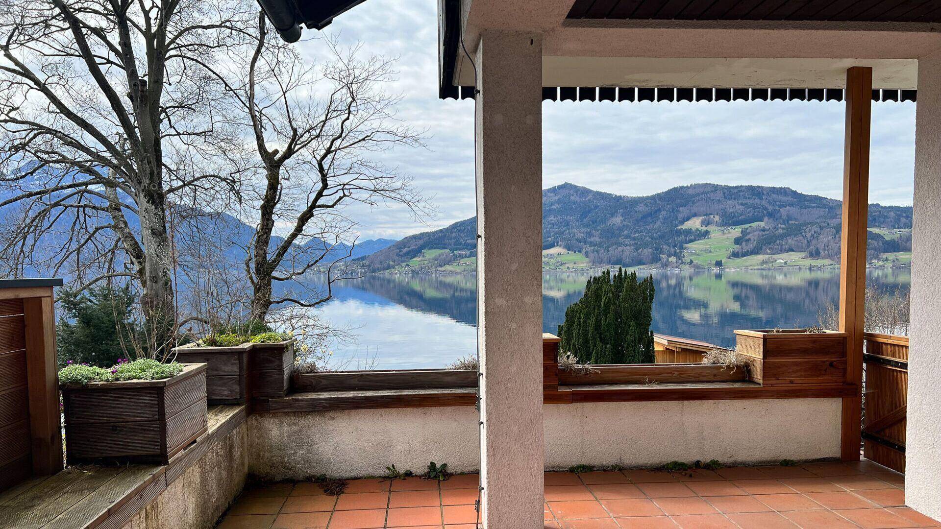 Überdachte Terrasse mit Terrakottafliesen, Pflanzenkübeln und weitem Blick auf den See und die Berge.