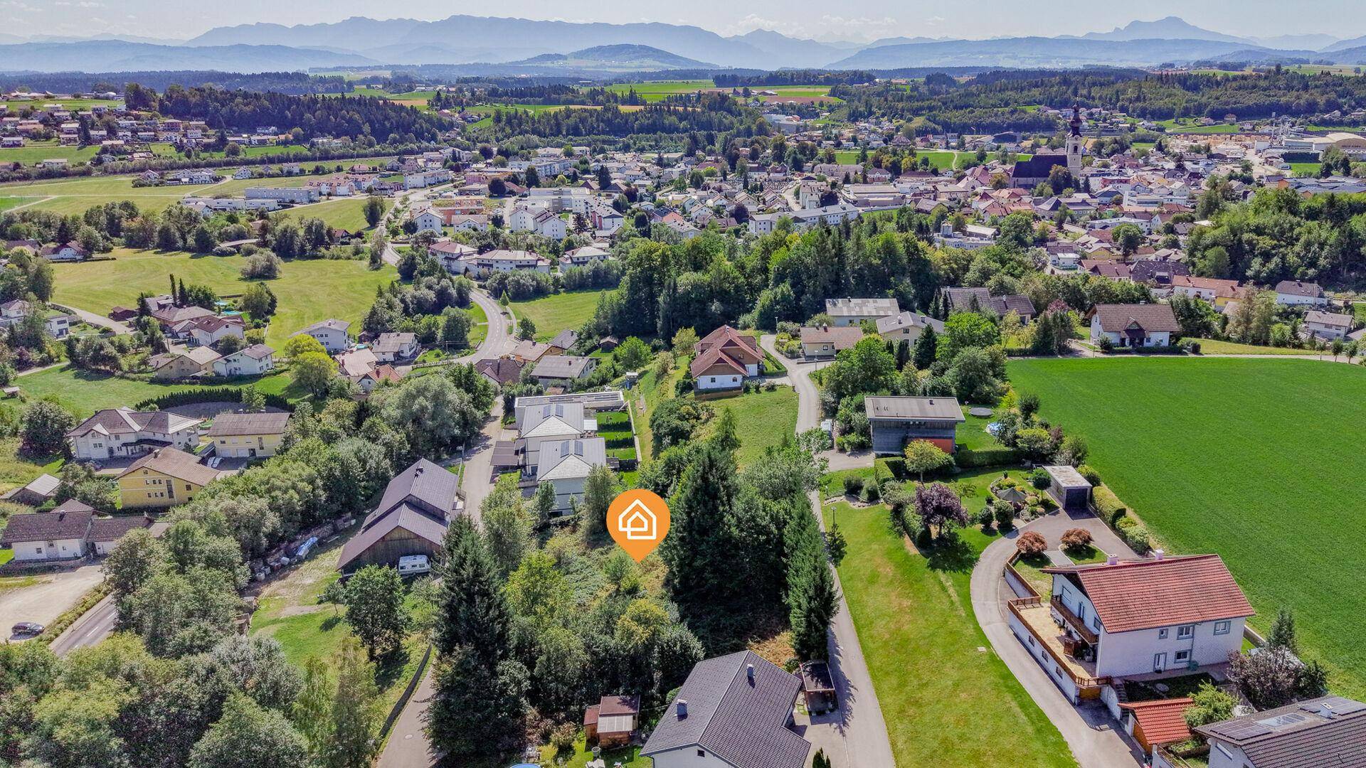 Weitläufige Luftaufnahme der Umgebung mit einer Stadt im Hintergrund und einer Bergkette am Horizont.