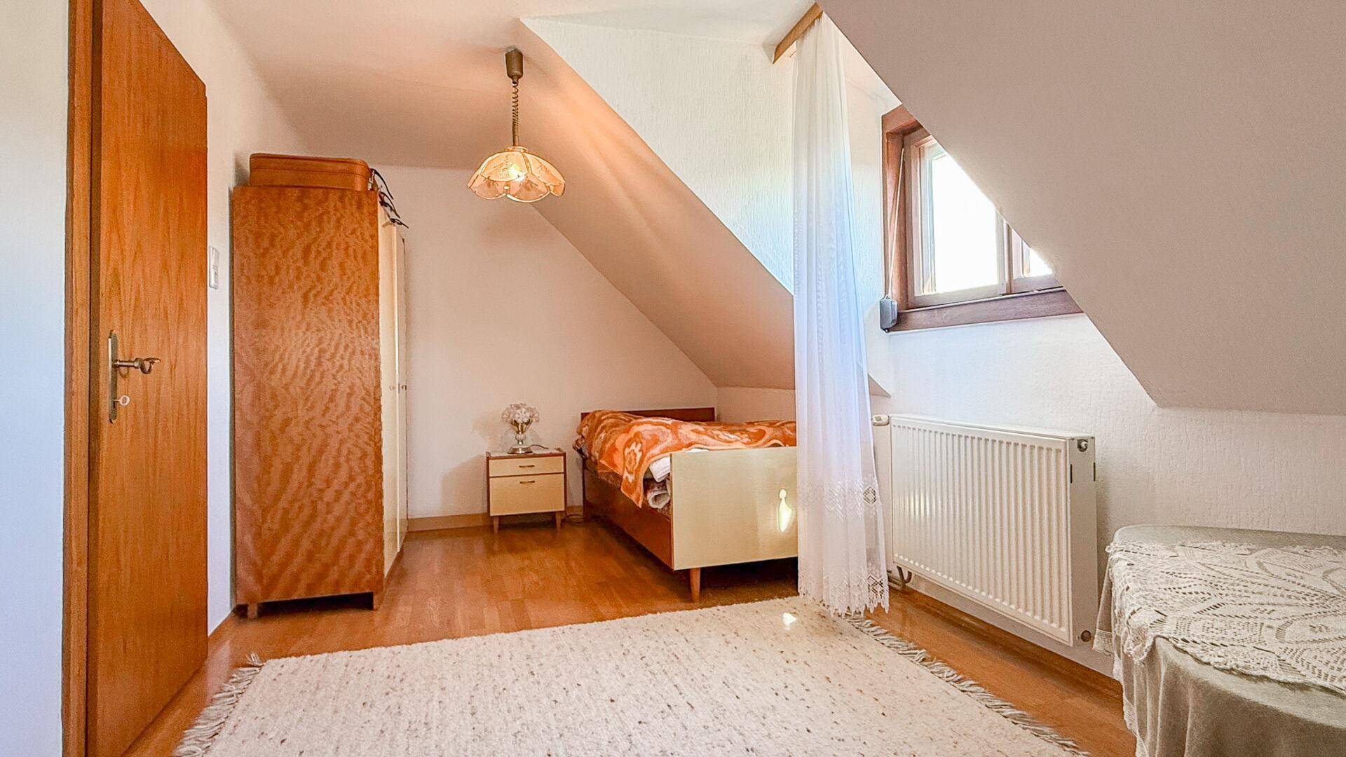 Helles Schlafzimmer im Dachgeschoss mit Einzelbett, Kleiderschrank und schräger Decke.