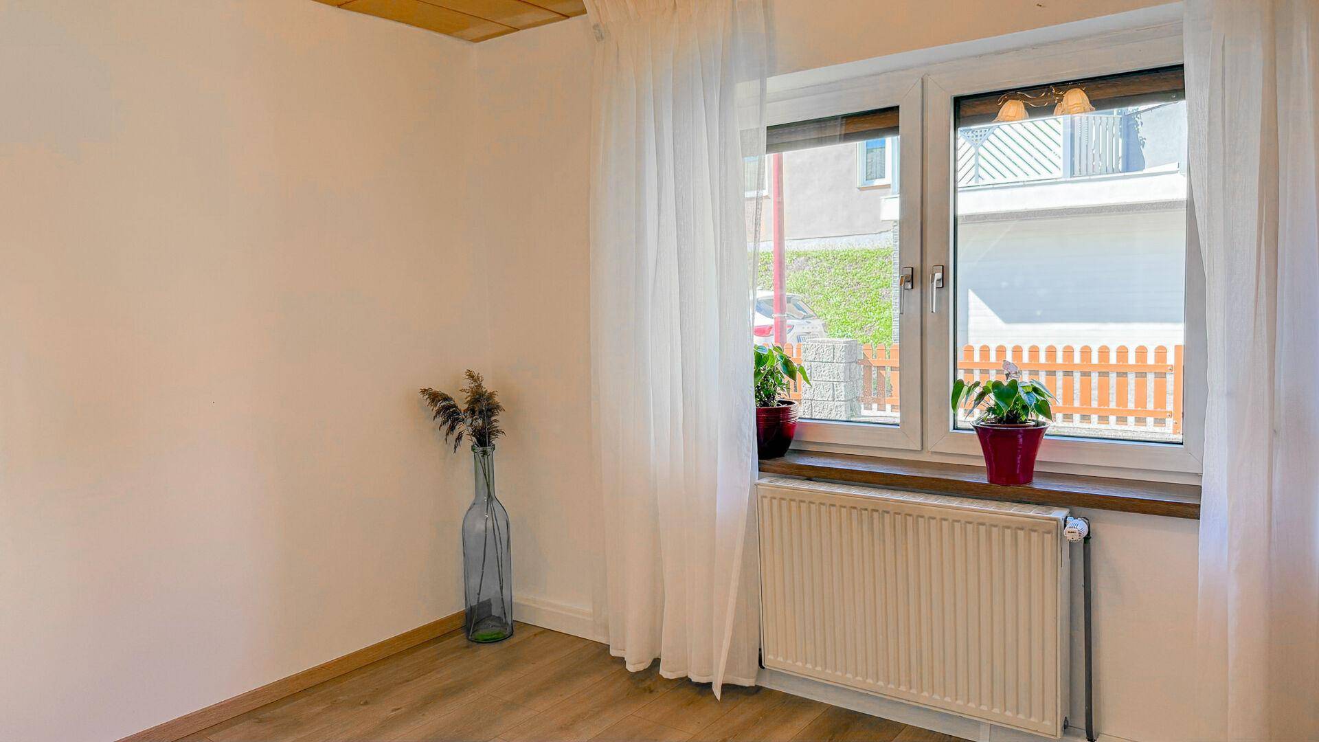 Heller, leerer Raum mit großem Fenster, Heizkörper und schlichten weißen Wänden.