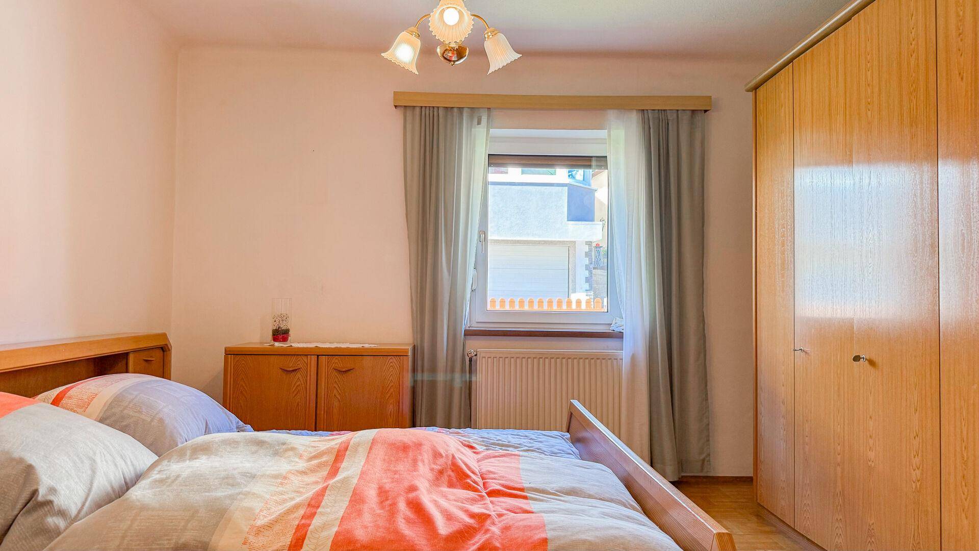 Schlafzimmer mit Doppelbett, Holzschrank und Fenster mit Blick auf die Umgebung.