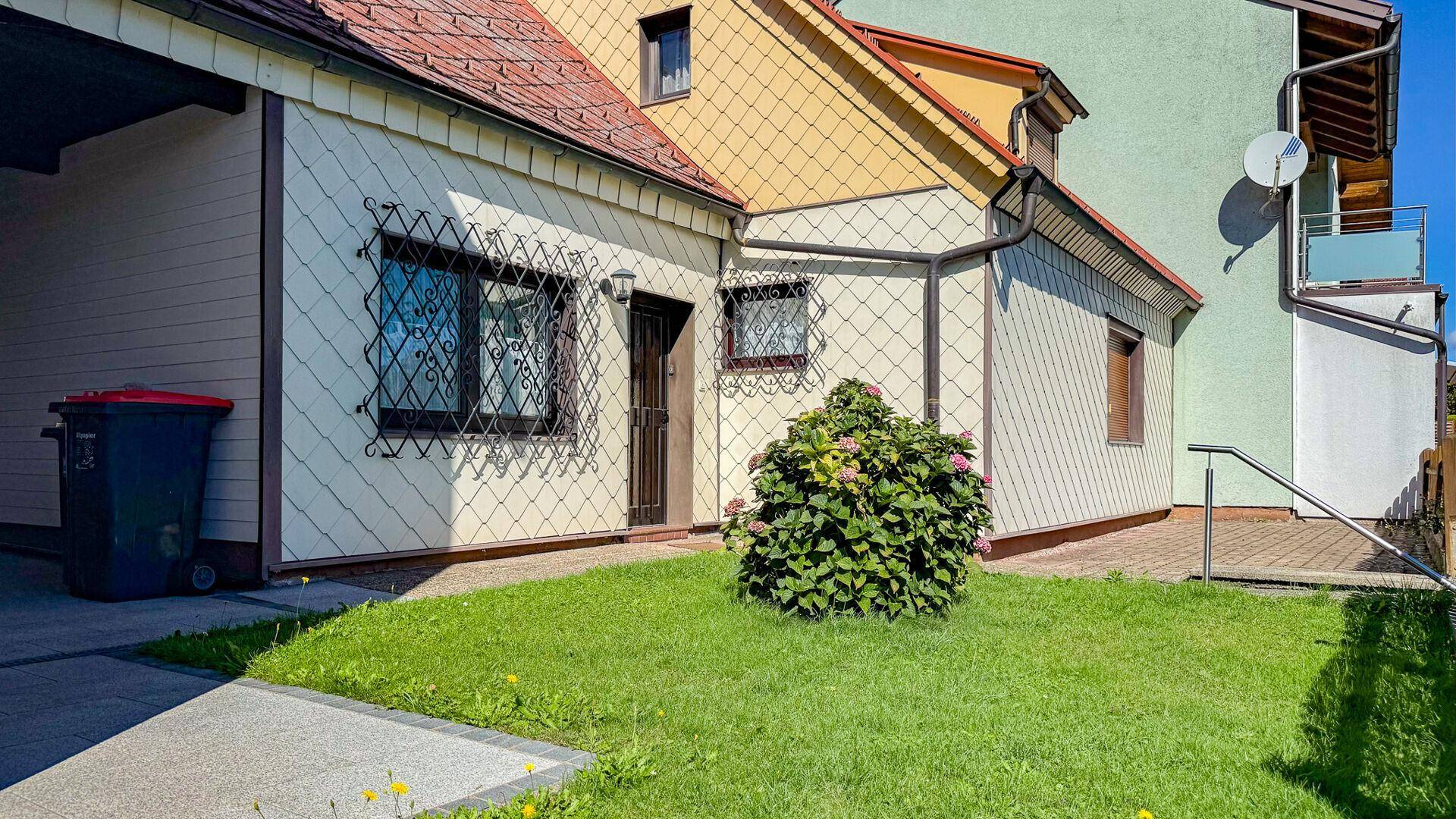 Seitenansicht des Hauses mit kleinem Vorgarten, dekorativen Fenstergittern und Zugang zum Carport.