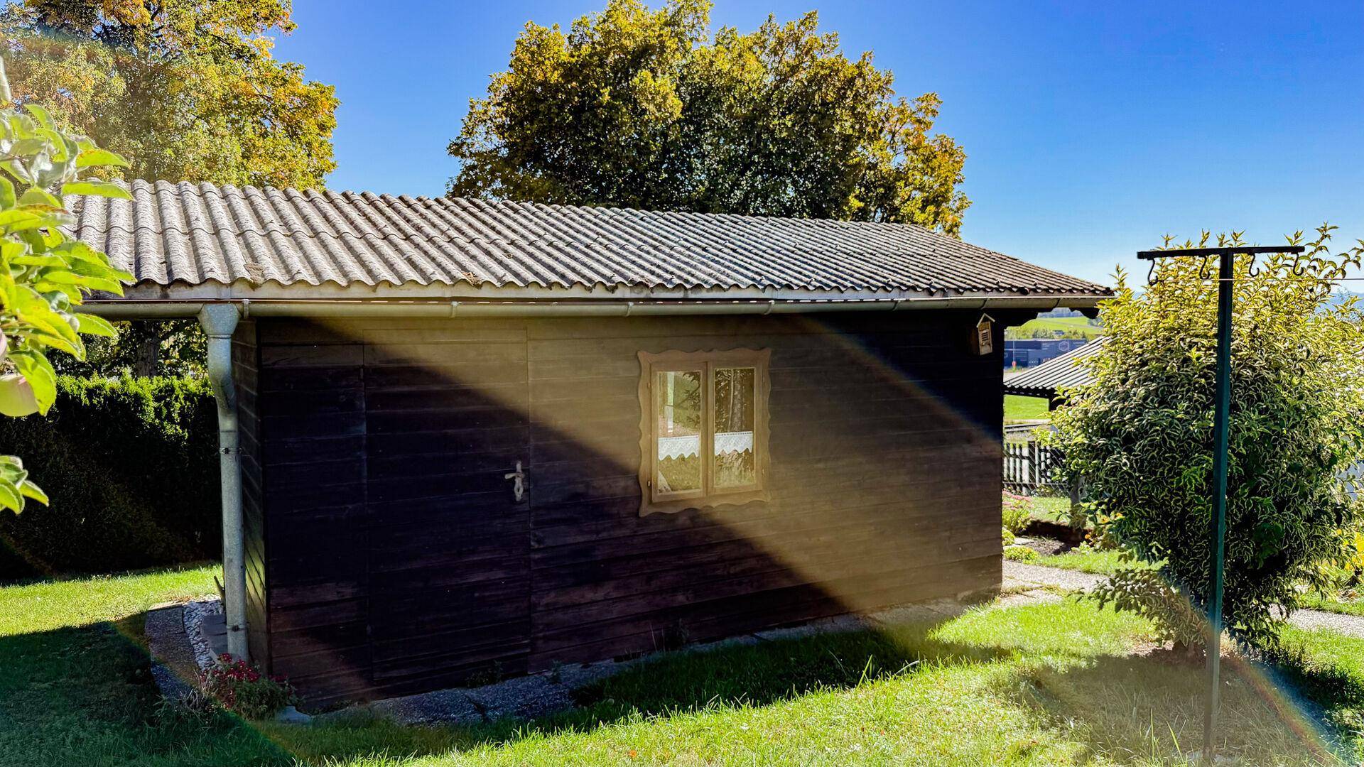 Rustikaler Holzschuppen im Garten mit kleinem Fenster und traditionellem Wellblechdach.