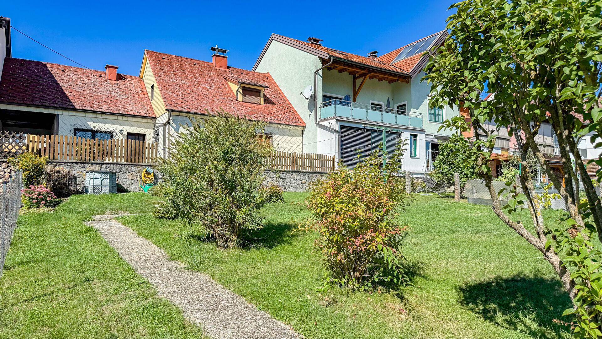 Gepflegter Garten mit Rasen, Sträuchern und Blick auf die Rückseite des Hauses und Nachbargebäude.