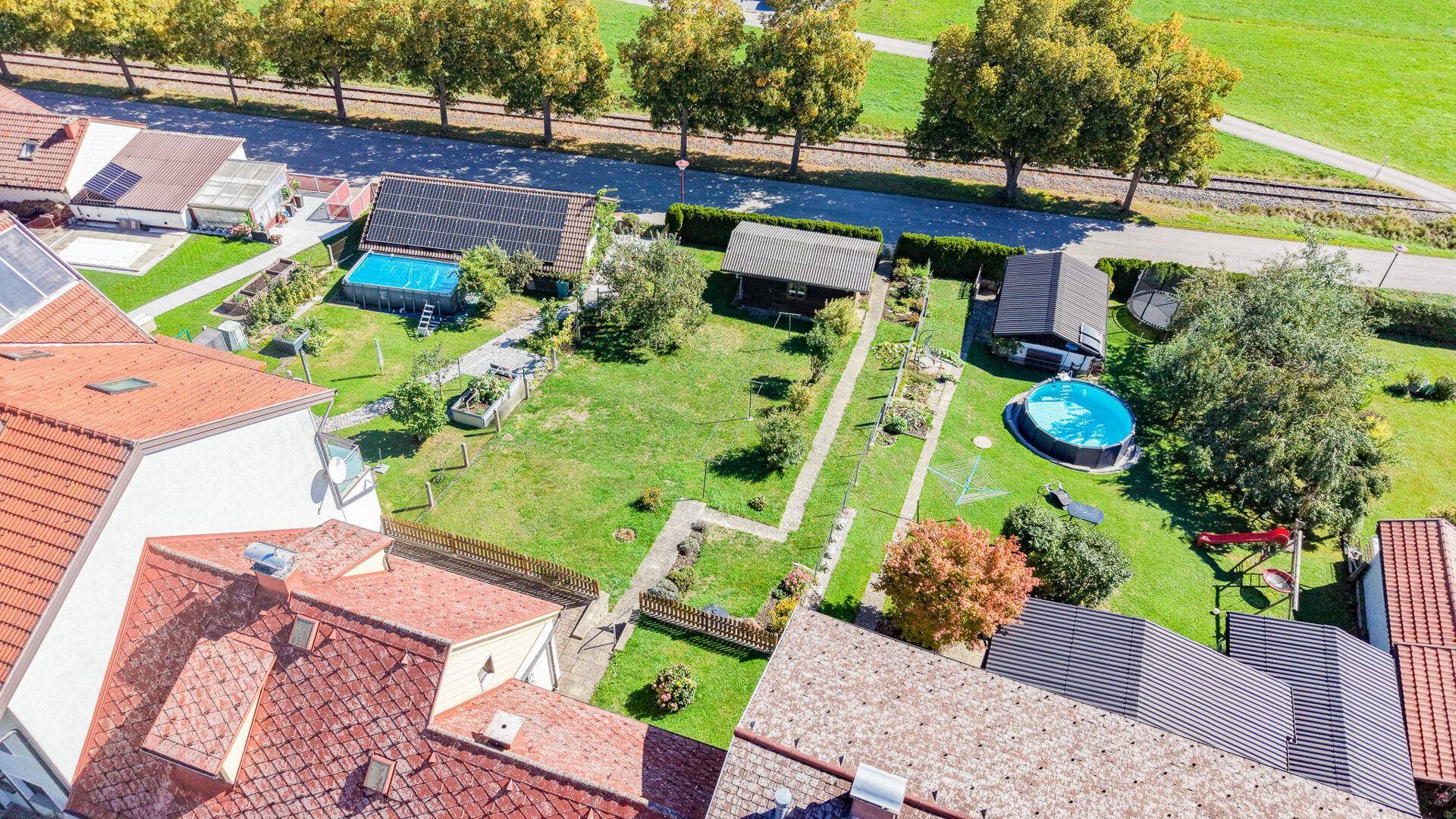 Vogelperspektive des Grundstücks mit Garten, Pool, Nebengebäuden und angrenzender Straße.