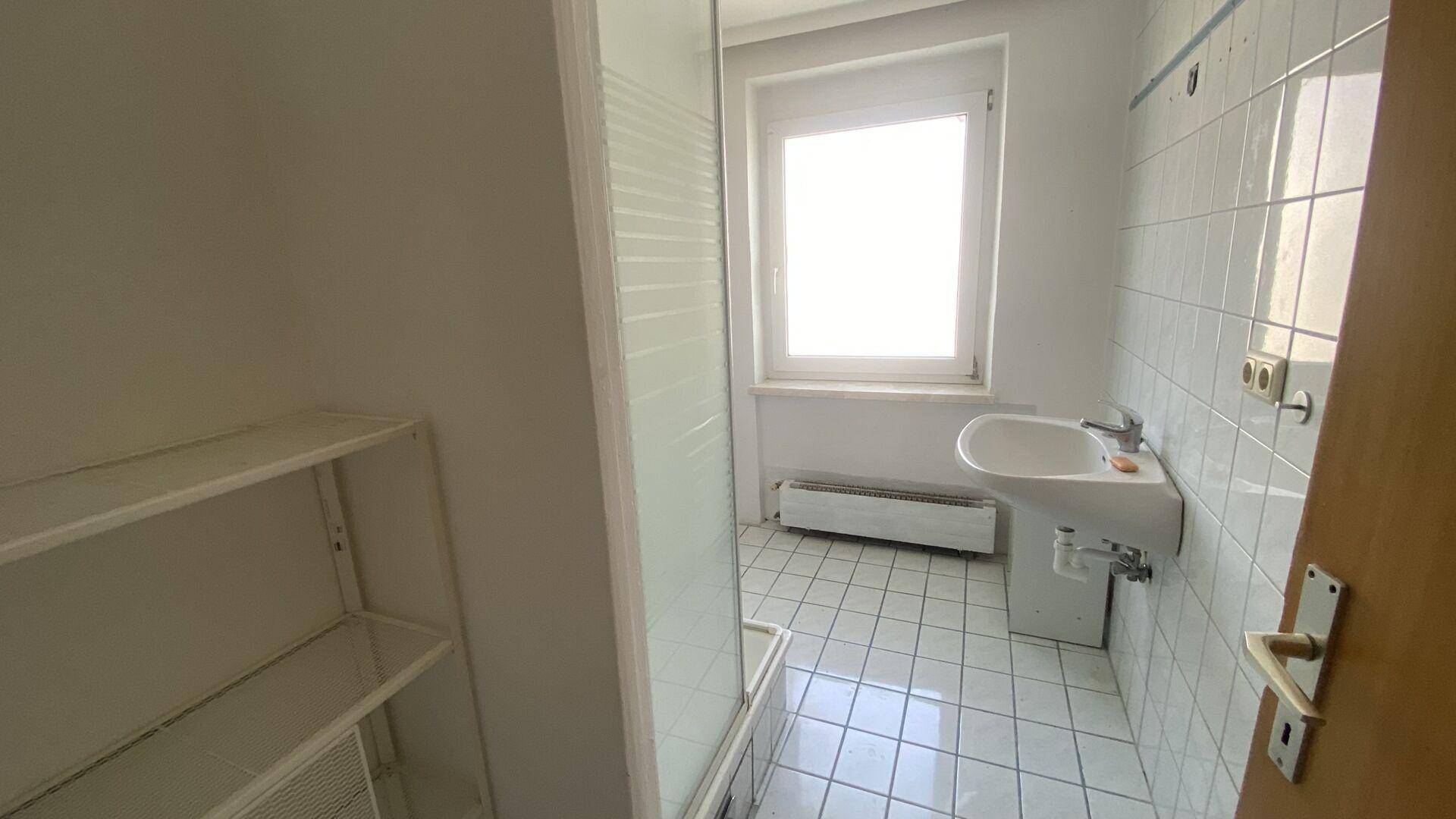 Badezimmer mit Duschkabine, Waschbecken und Fenster für natürliche Belüftung und Licht.