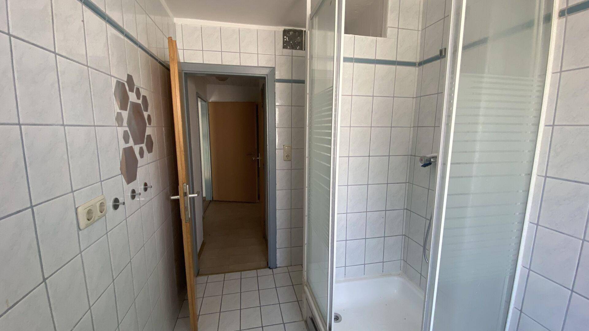 Gefliestes Badezimmer mit Duschkabine und einfacher Ausstattung, funktional und hell.