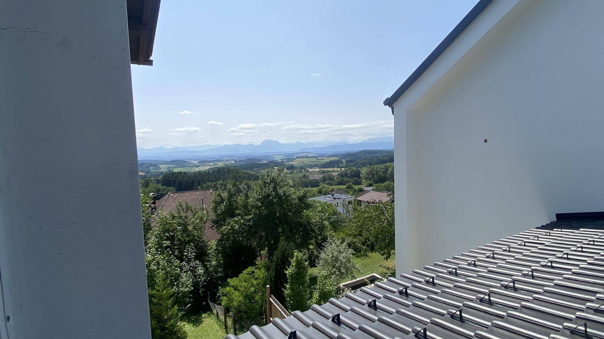 Weitläufiger Blick über die grüne Landschaft und ferne Berge, eingerahmt von Gebäuden.