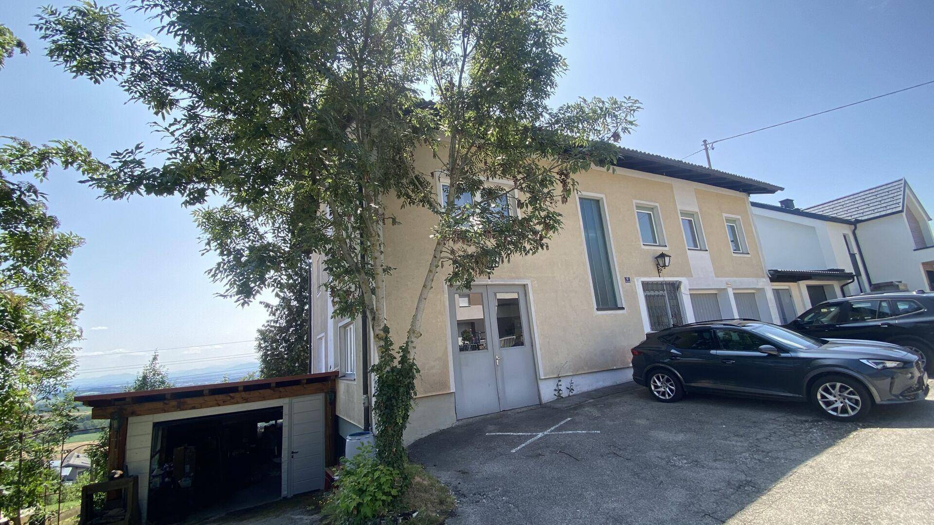 Außenansicht des Hauses mit Zufahrt, offener Garage und geparktem Auto auf dem Grundstück.