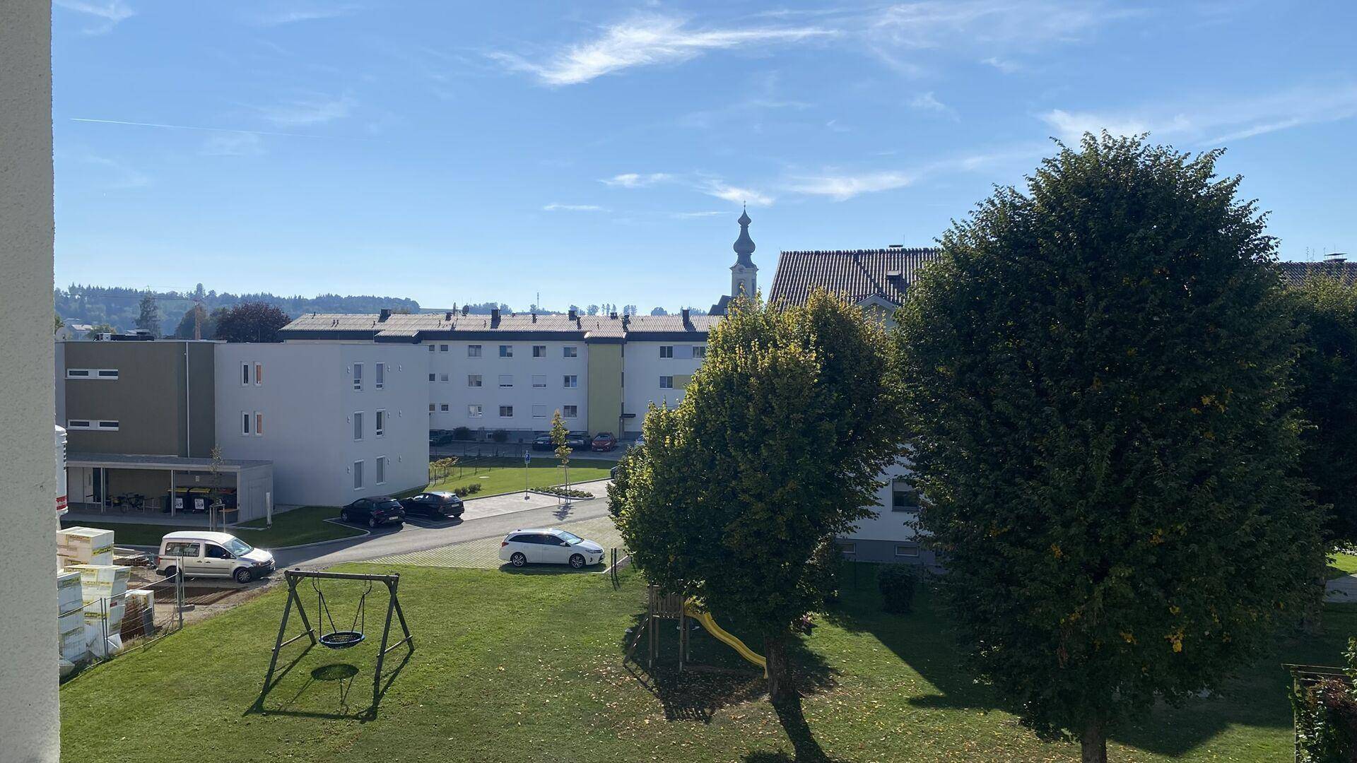 Weitläufiger Blick auf die grüne Umgebung mit Spielplatz und Wohngebäuden unter klarem Himmel.