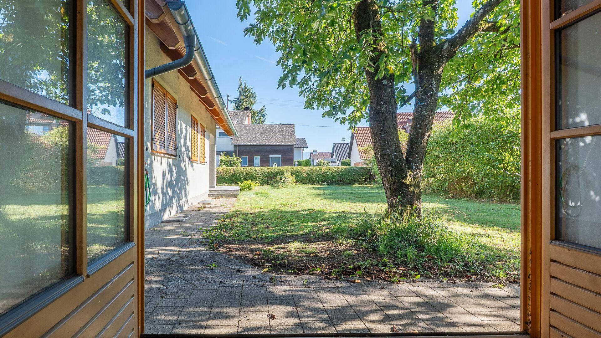 Blick durch offene Türen auf eine gepflasterte Terrasse und den grünen Gartenbereich.