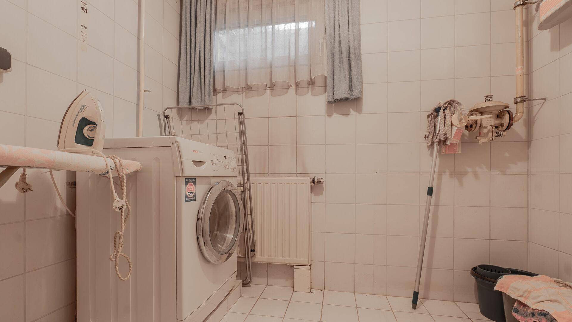 Praktischer Hauswirtschaftsraum im Keller mit Waschmaschine, Bügelbrett und gefliesten Wänden.