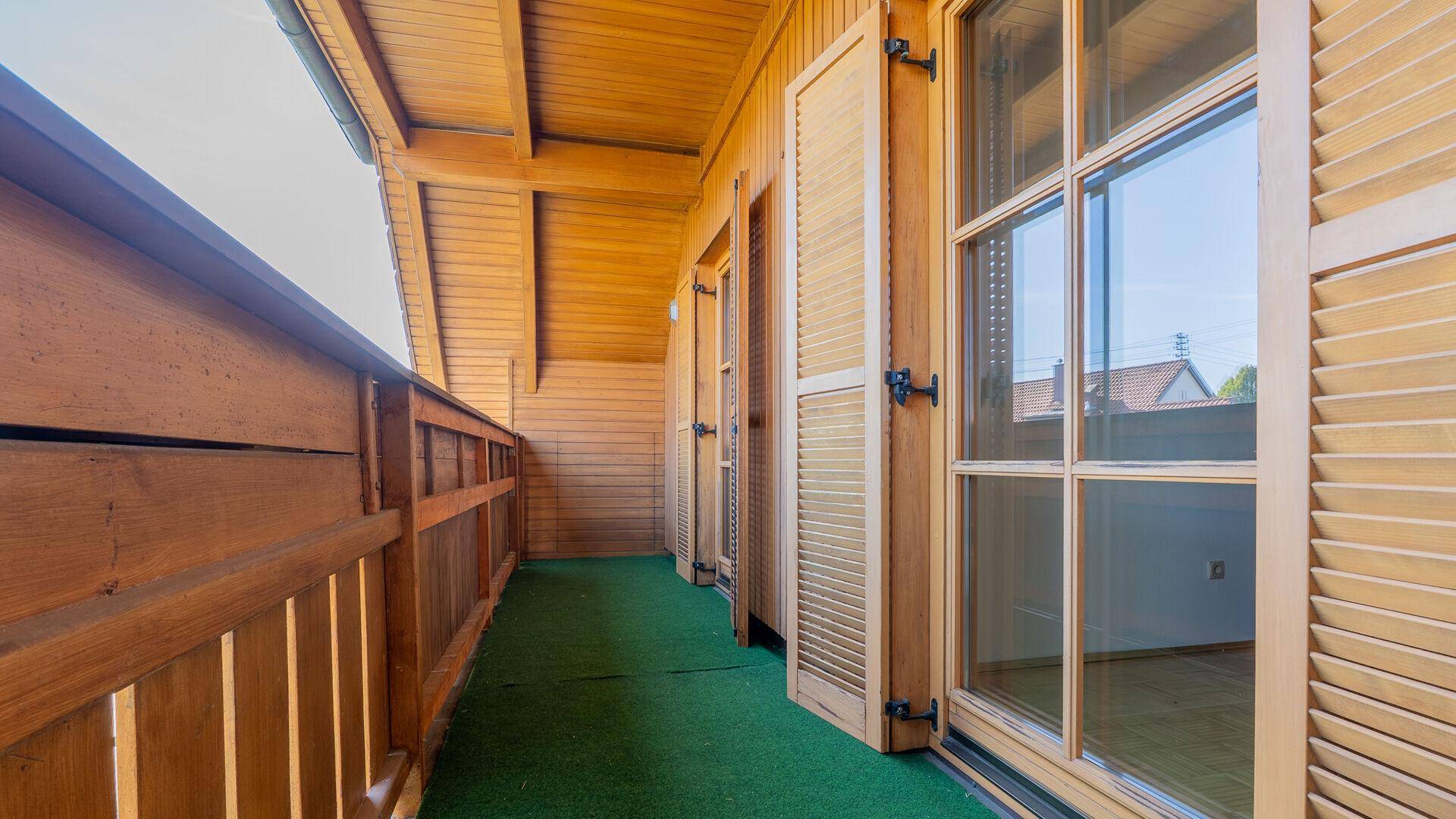 Langer Holzbalkon mit Kunstrasen und Holzverkleidung, ideal für entspannte Stunden im Freien.