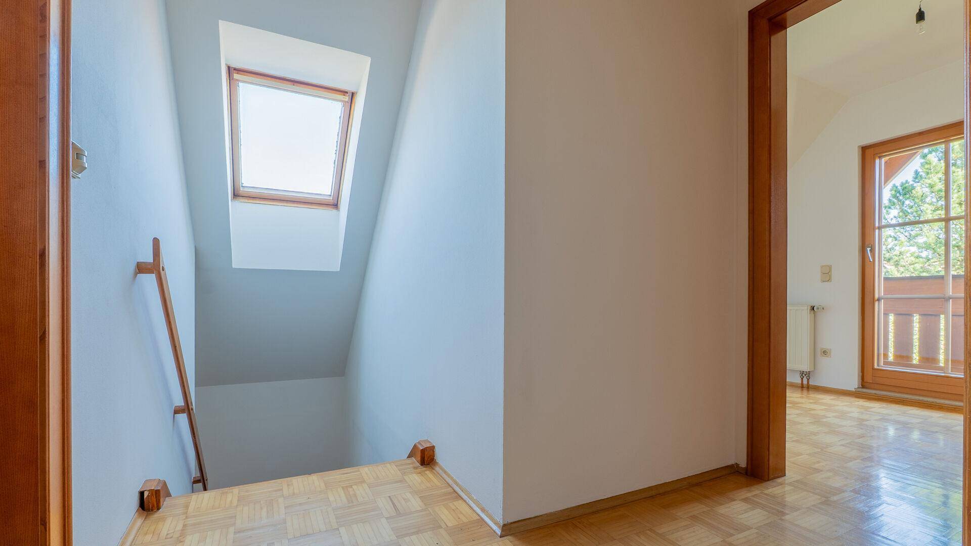 Treppenaufgang zum Obergeschoss mit Dachfenster, das für natürliche Belichtung sorgt.
